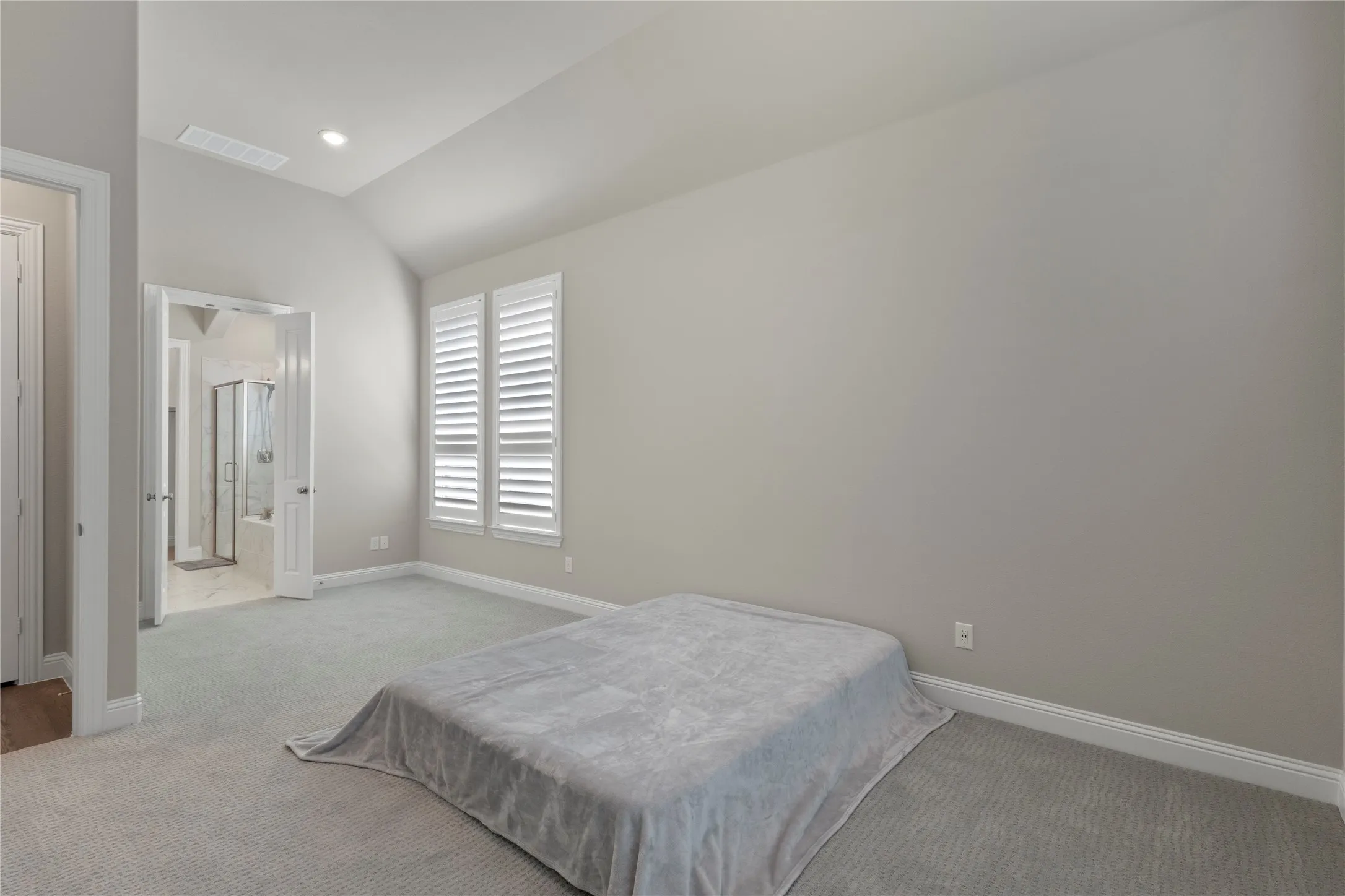 Vaulted ceilings, neutral carpeting, and windows fitted with plantation shutters