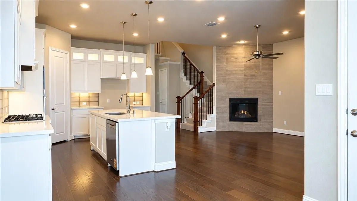 Kitchen featuring white shaker-style cabinetry, quartz countertops, a central island, recessed lighting, and wood-finish flooring, complemented by a floor-to-ceiling stone-tiled fireplace
