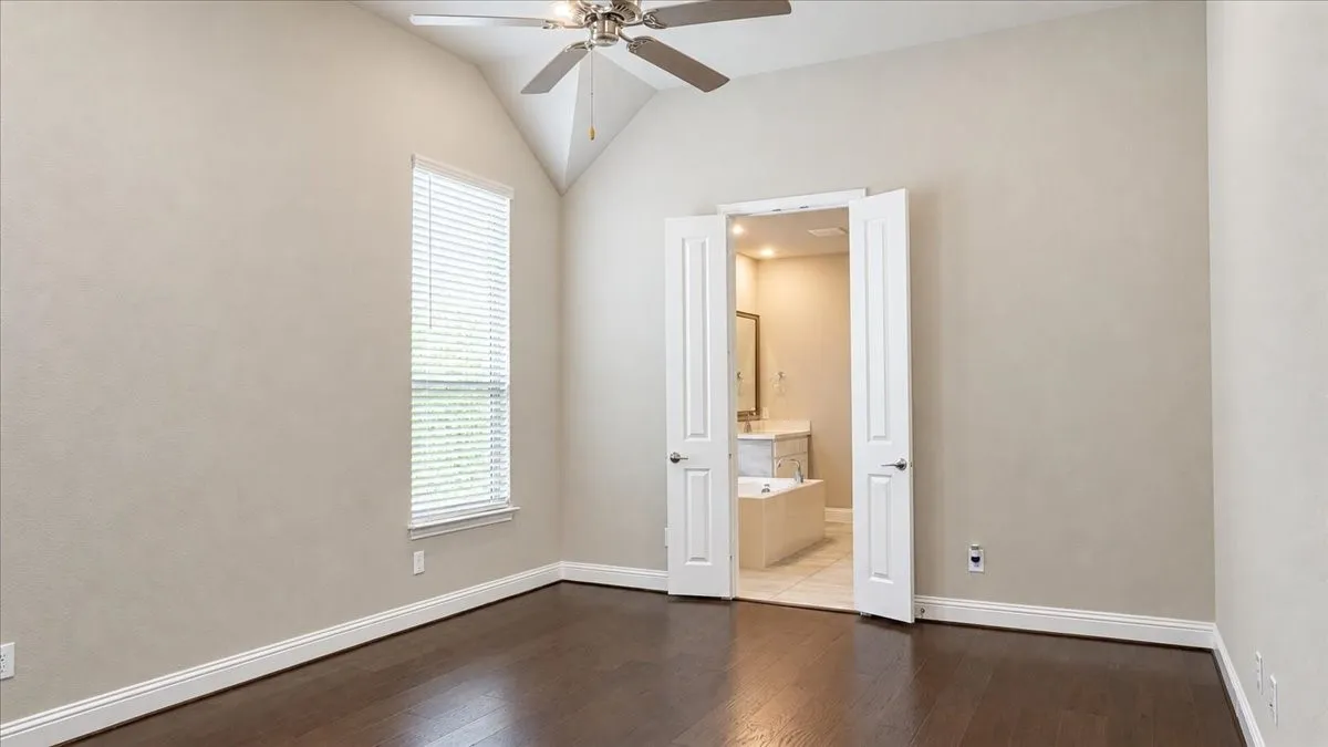 Vaulted ceiling featuring a central brushed-nickel ceiling fan, rich wood-finish flooring, and double-door entry