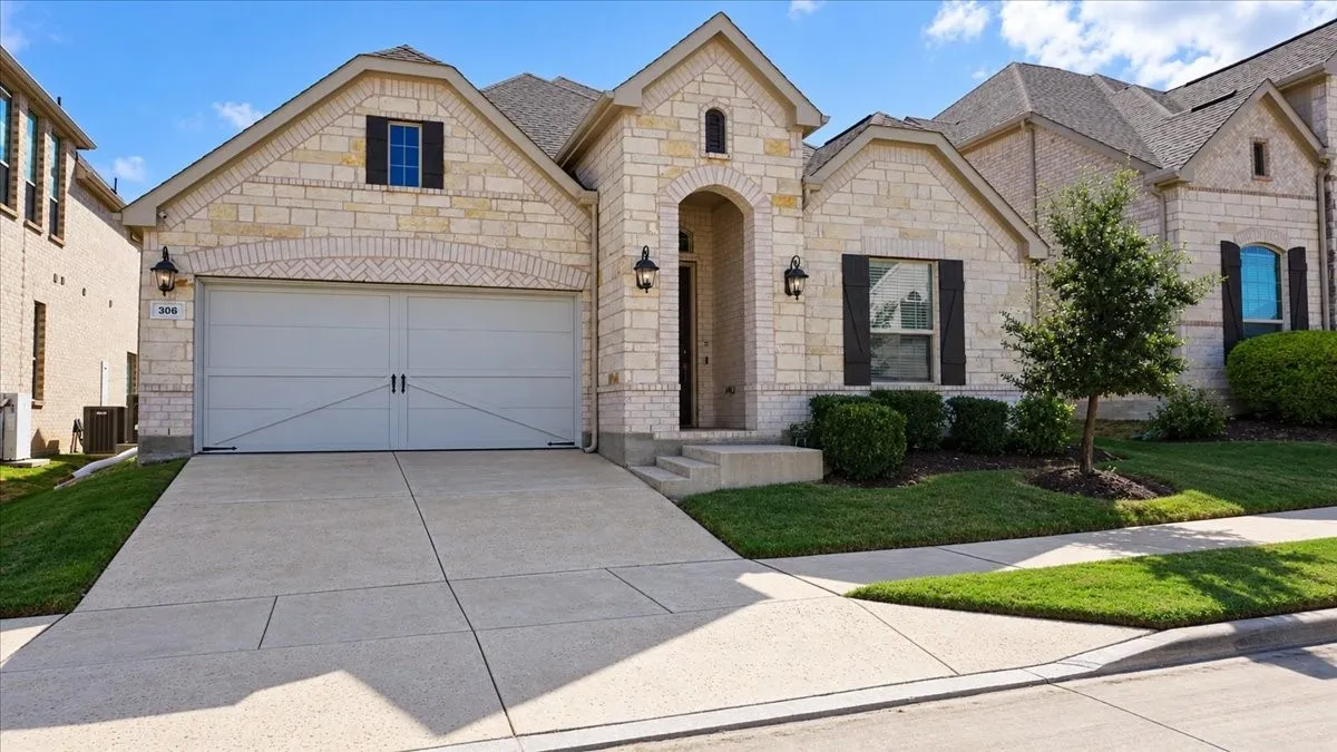 Stone and brick facade featuring a multi-gabled roofline, an arched entryway, decorative shutters, and an attached two-car garage