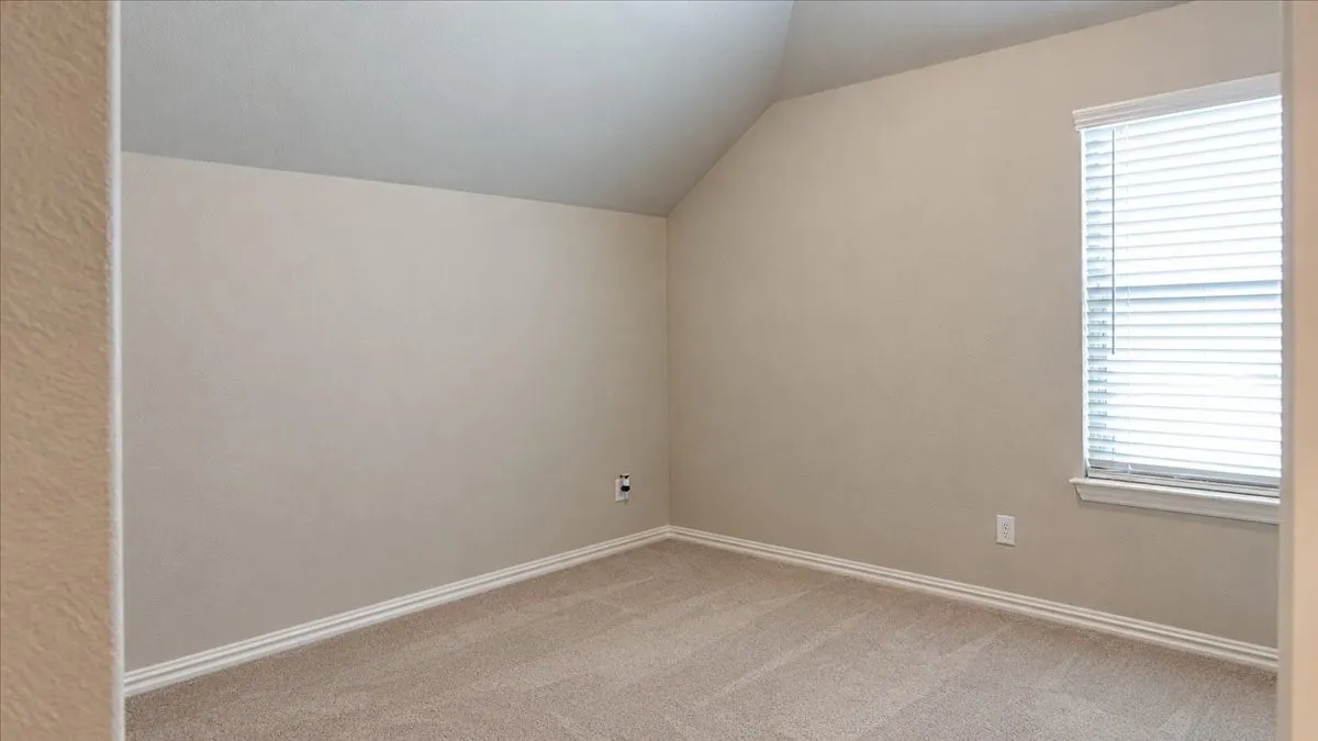 Neutral-toned room featuring vaulted ceilings, neutral carpeting, and a window with horizontal blinds