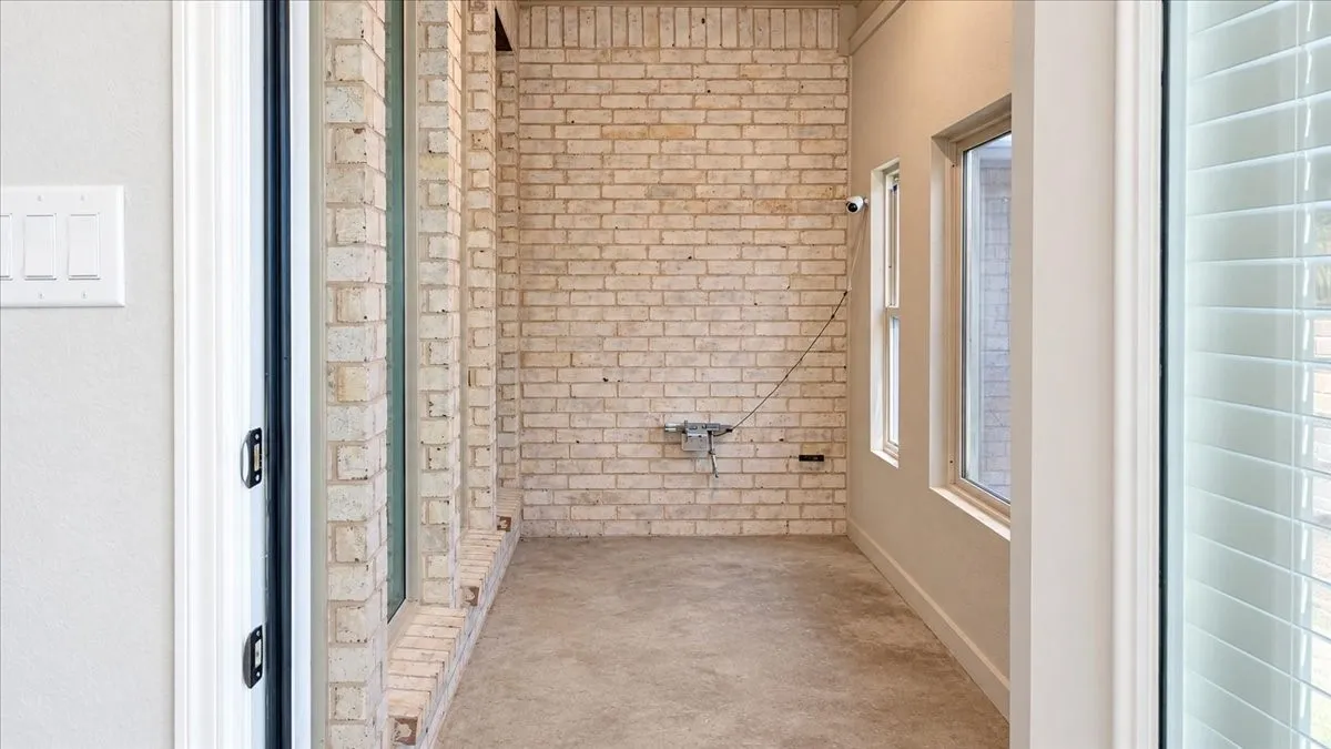 Enclosed porch featuring an exposed light-toned brick accent wall, concrete flooring, and multiple windows