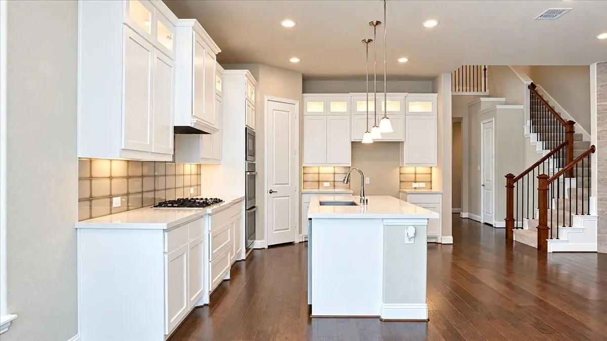 Kitchen featuring white shaker cabinetry, quartz countertops, a central island with an integrated sink, built-in double wall ovens, and wood-finish flooring