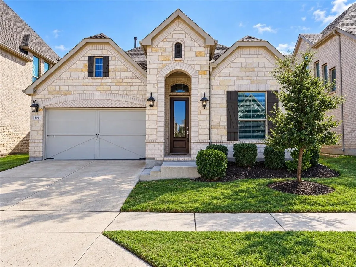 Stone facade exterior featuring a gabled roofline, arched entryway, two-car garage with carriage-style detailing, and decorative shutters