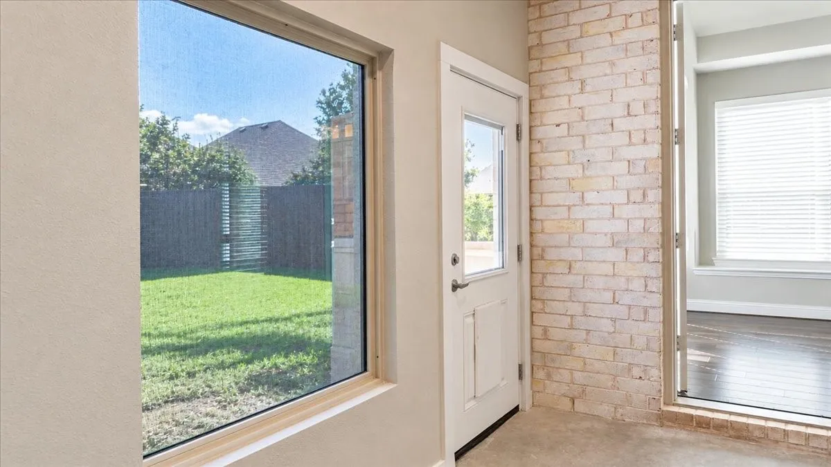 Exposed light-toned brick wall, large picture window, and exterior door with glass inlay