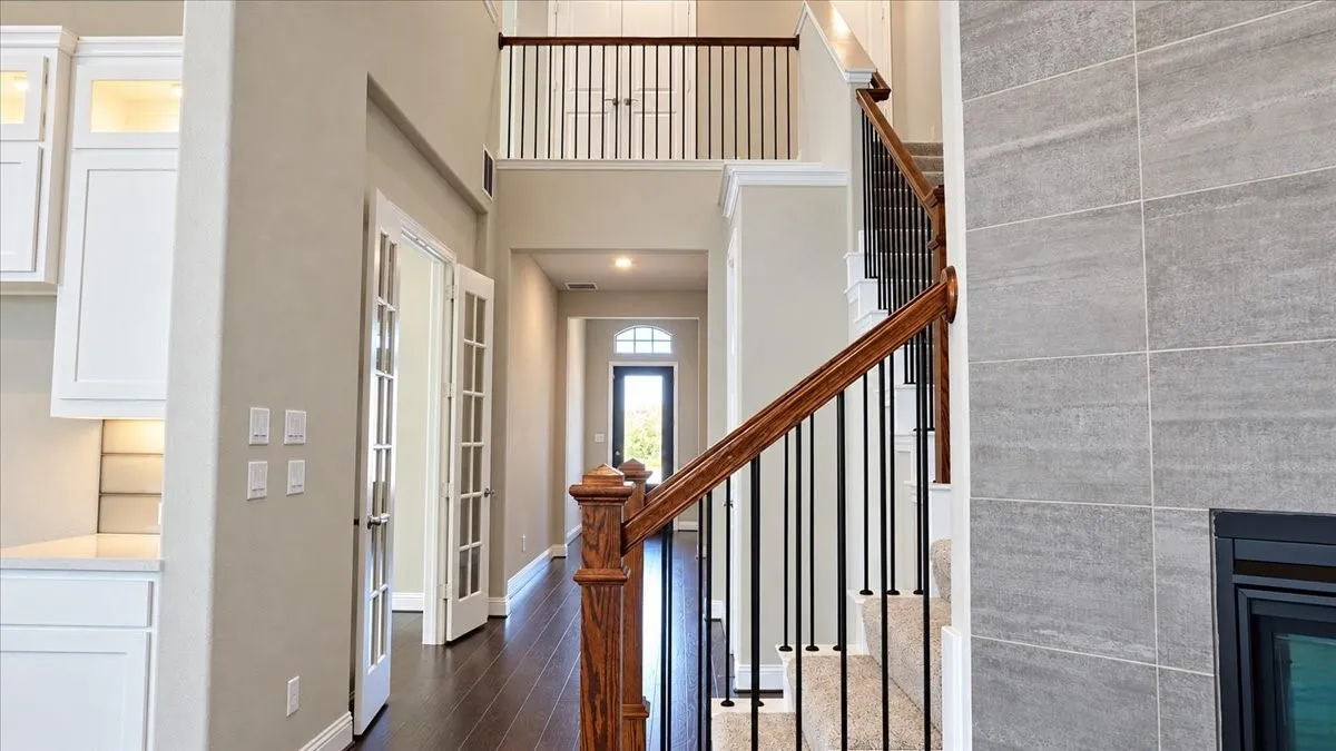 Two-story foyer featuring dark wood-finish flooring, a wood-railed staircase with metal balusters, and a floor-to-ceiling stone fireplace surround