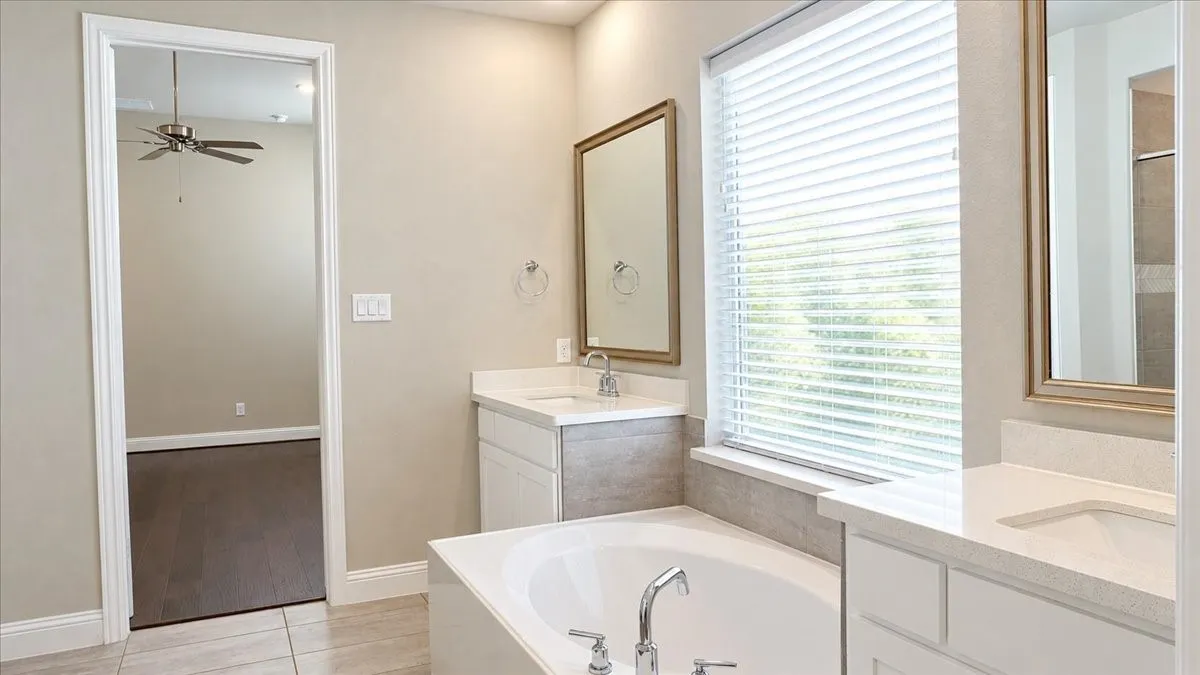 Bathroom featuring dual vanities with solid-surface countertops, soaking tub, tile flooring, and framed mirrors