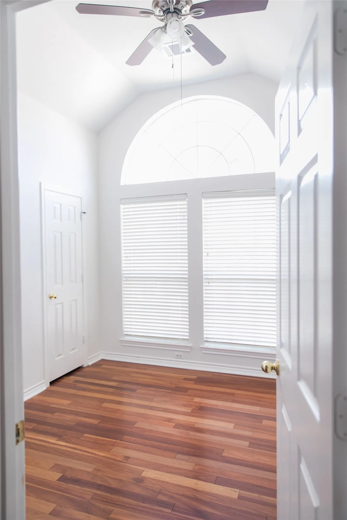 Vaulted ceilings featuring an arched window, wood-finish flooring, and a ceiling-mounted fan with integrated lighting