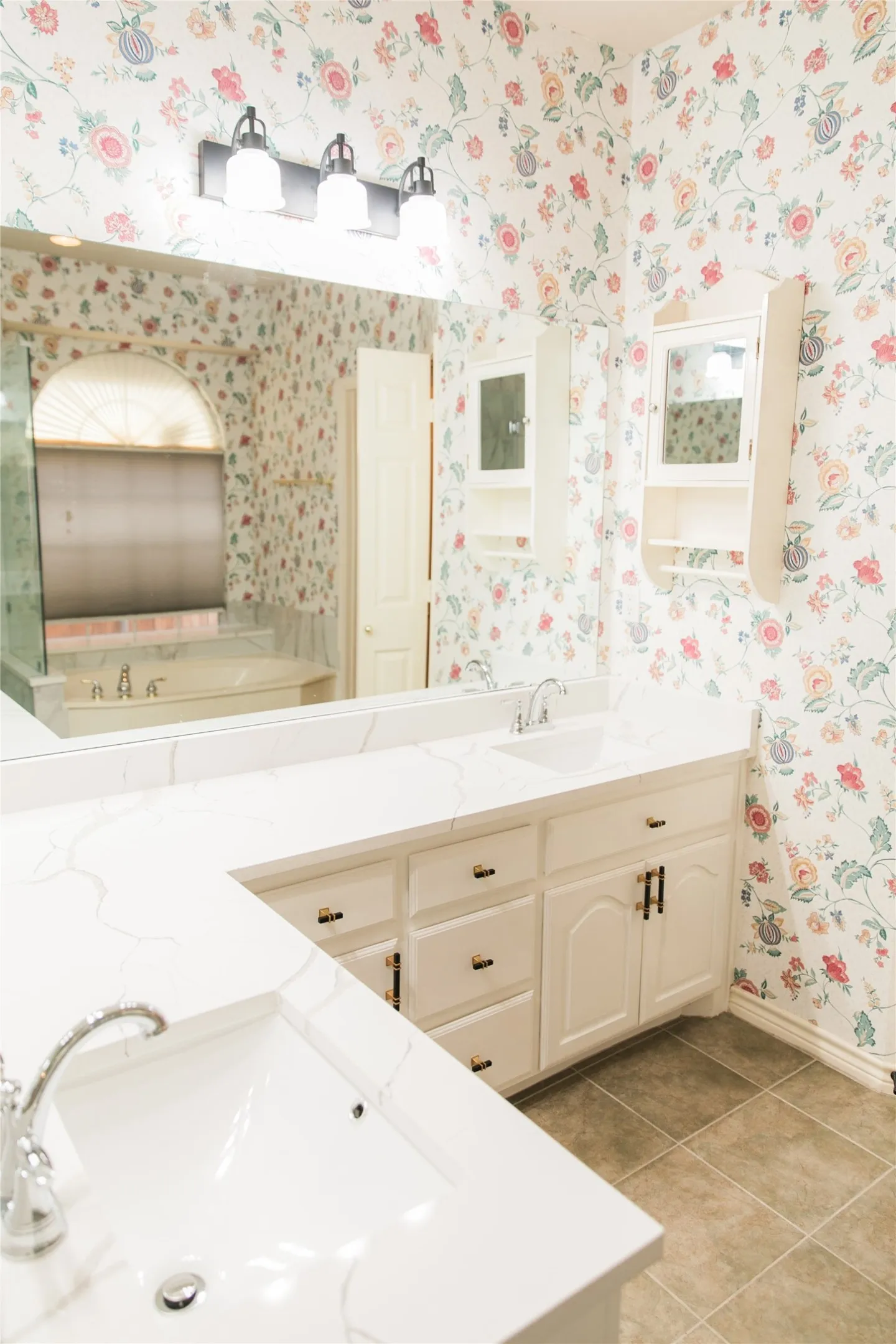 Dual-sink vanity featuring white cabinetry, stone-finish countertops, wall-mounted storage, and a three-light fixture