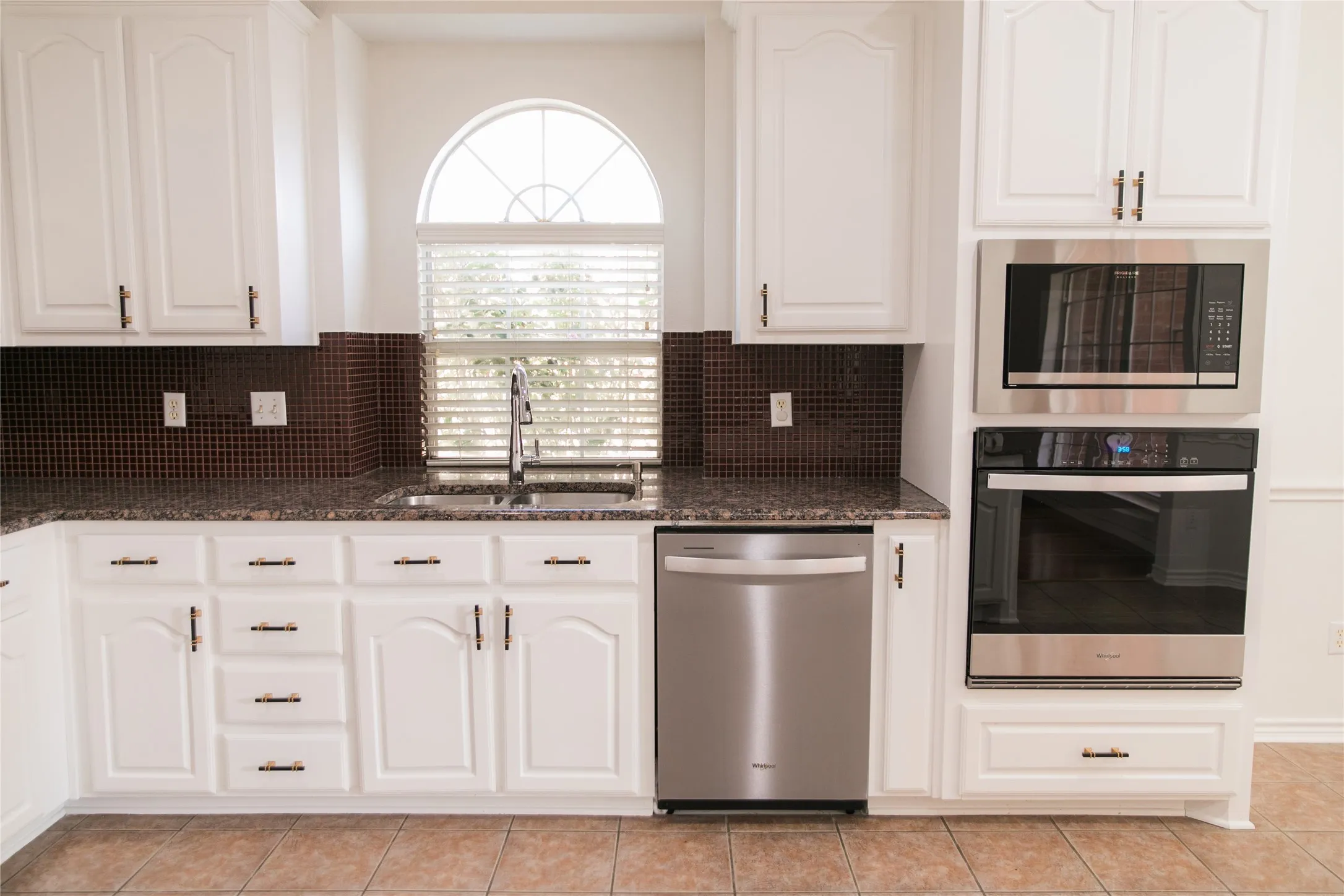 Kitchen featuring white cabinetry, stainless steel built-in double oven and microwave, stone-finish countertops, tiled backsplash, and an arched window