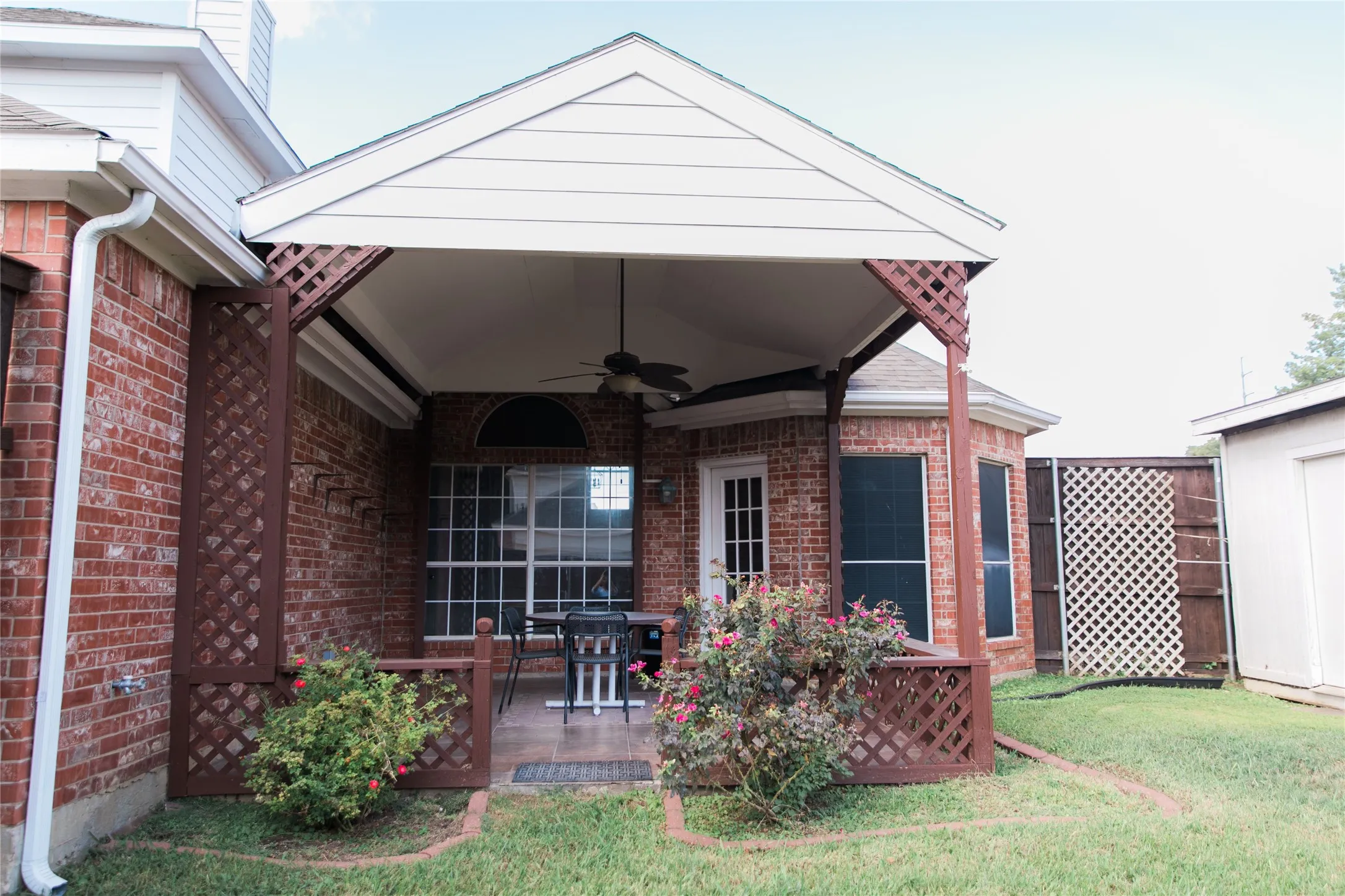Covered patio featuring a vaulted ceiling with an integrated fan, brick exterior, lattice privacy screening, and tile flooring