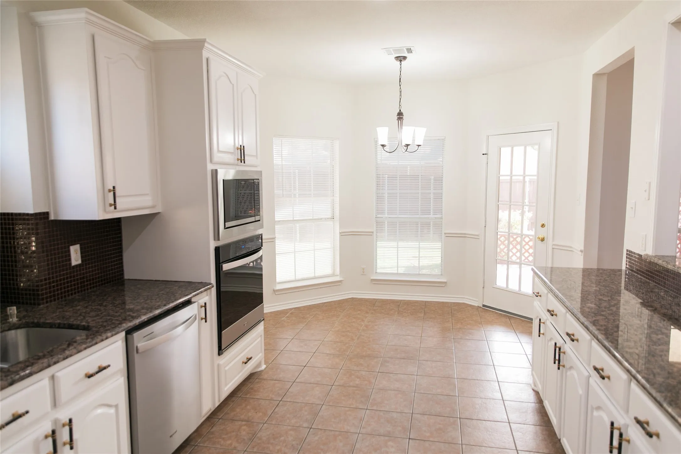 Kitchen featuring white cabinetry, stone countertops, integrated stainless steel double oven, tile flooring, and bay window area