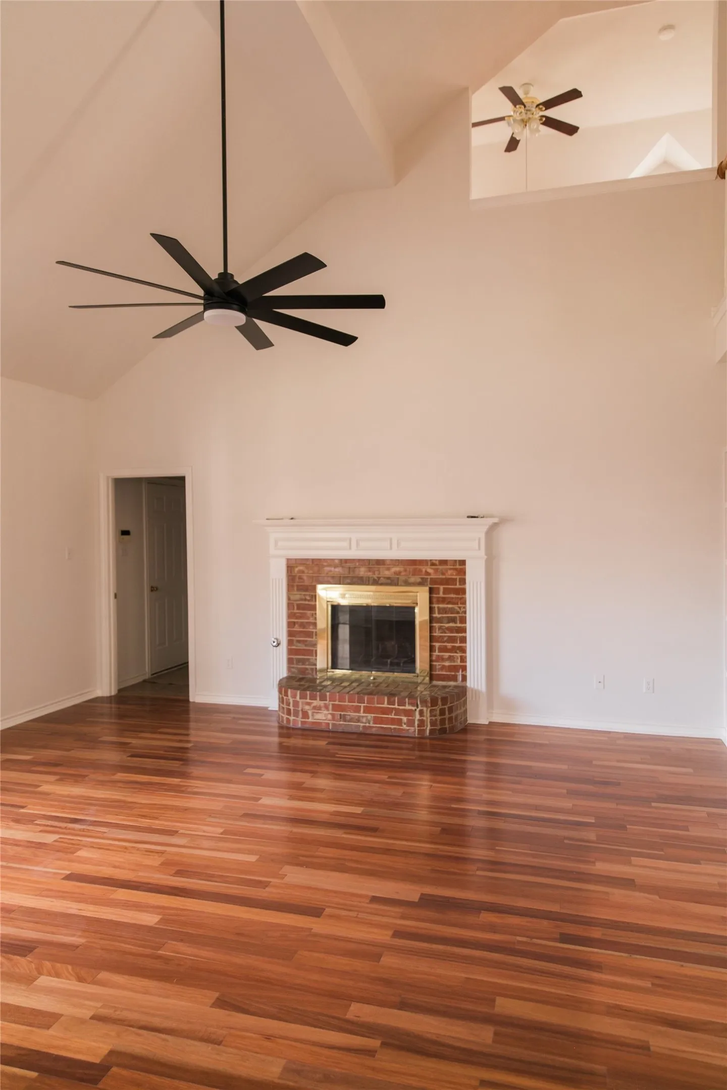 Vaulted ceilings, wood-finish flooring, brick fireplace with a custom mantel, and multi-blade ceiling fan