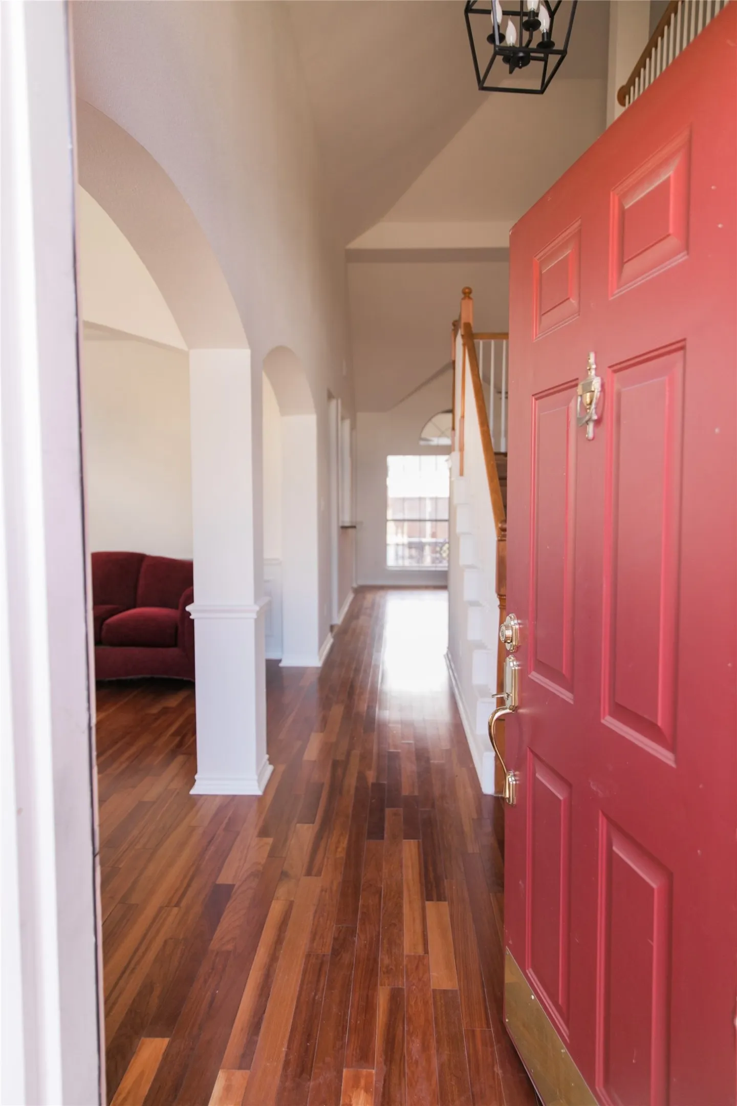 Foyer featuring wood-finish flooring, vaulted ceilings, arched architectural openings, and a staircase with a wooden handrail