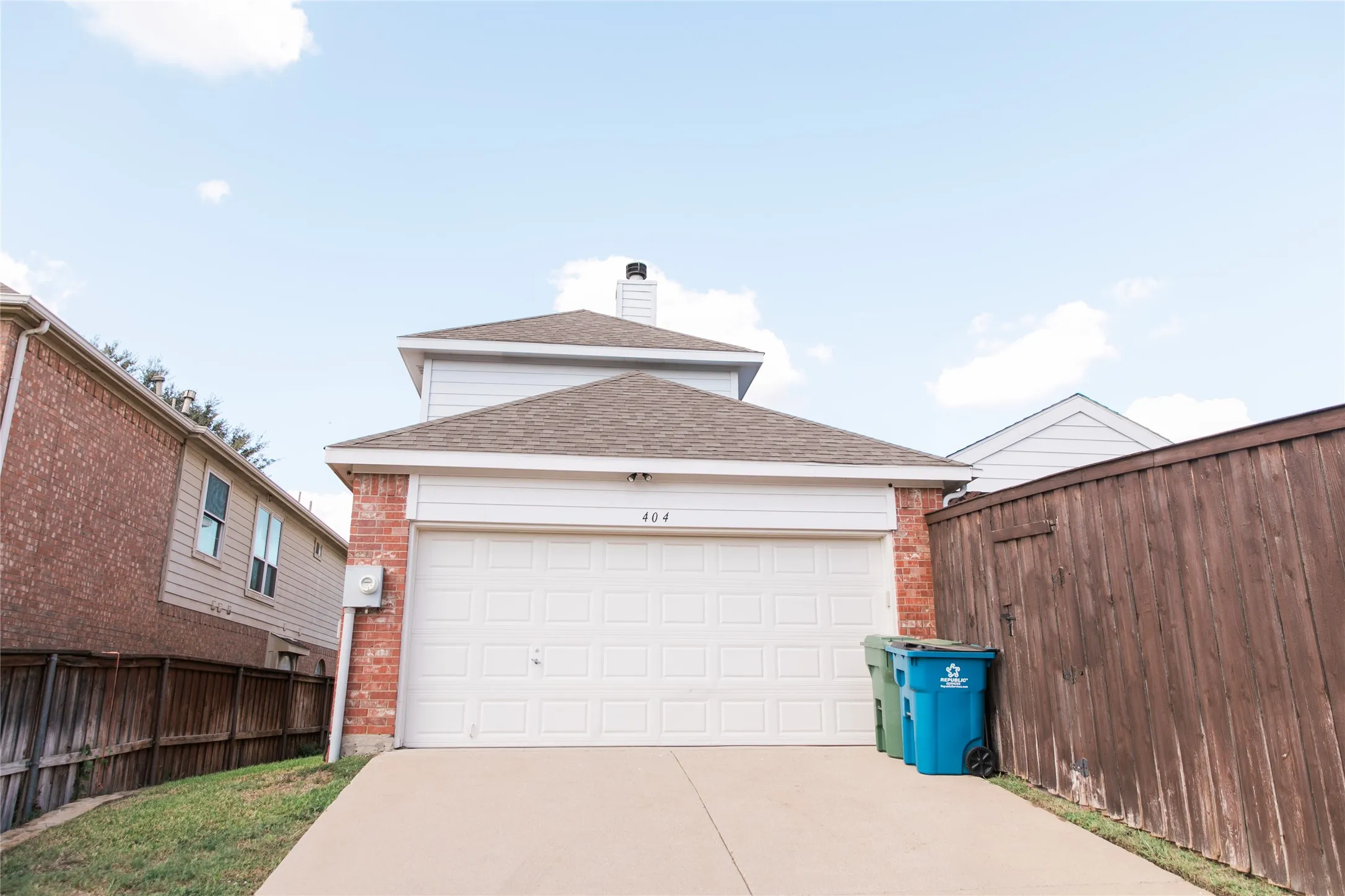 Two-story exterior featuring a brick and horizontal siding facade, shingle roof, chimney stack, and a two-car garage