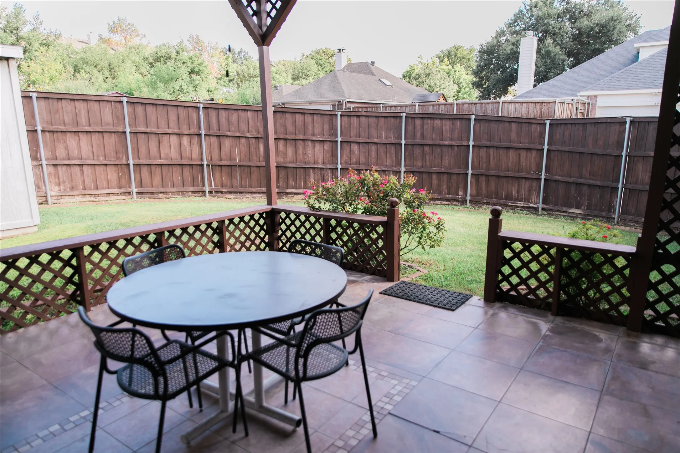Covered patio with tiled flooring, wood lattice perimeter railing, and a private fenced backyard