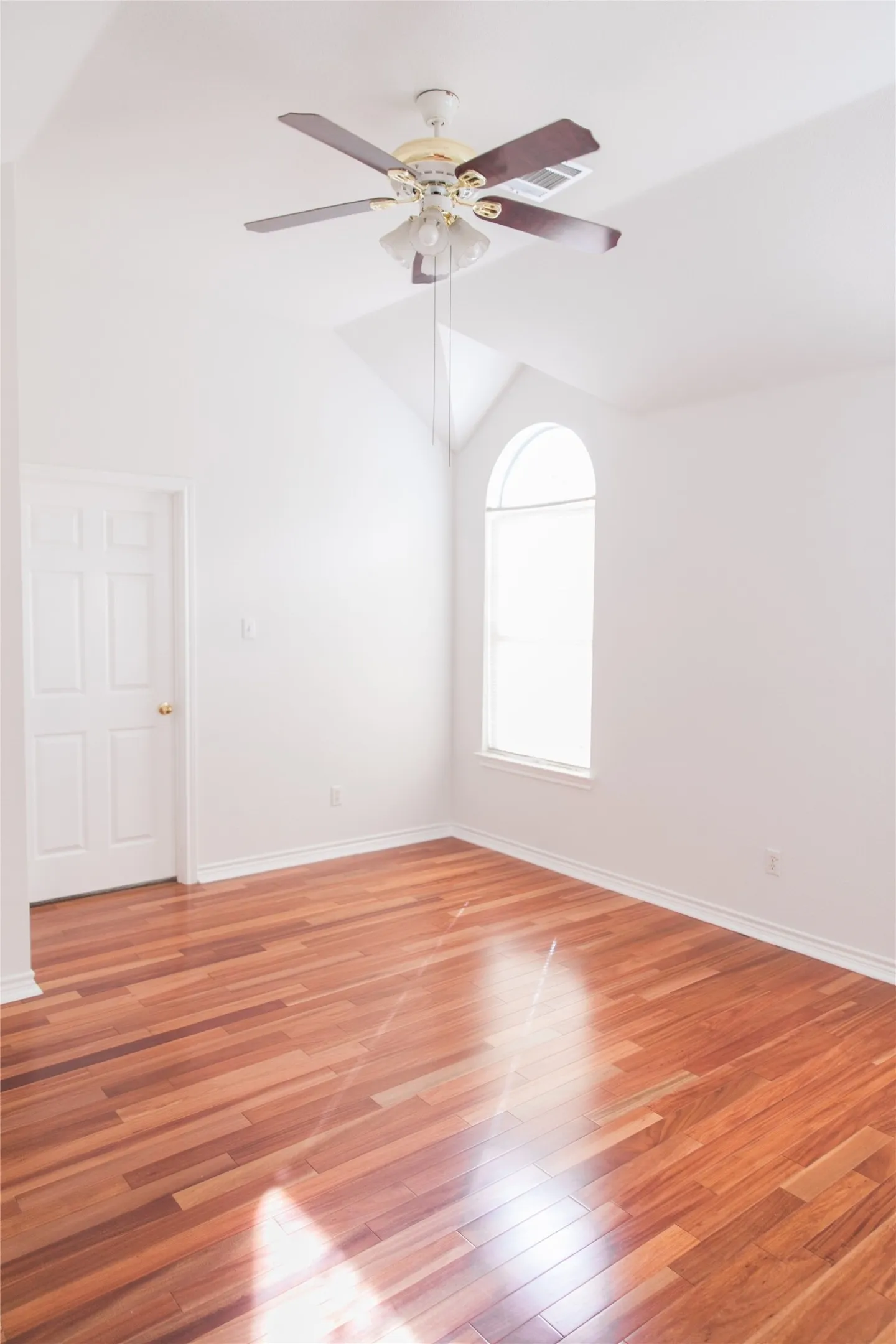Vaulted ceiling featuring an arched window, wood-finish flooring, and a multi-blade ceiling fan with integrated lighting