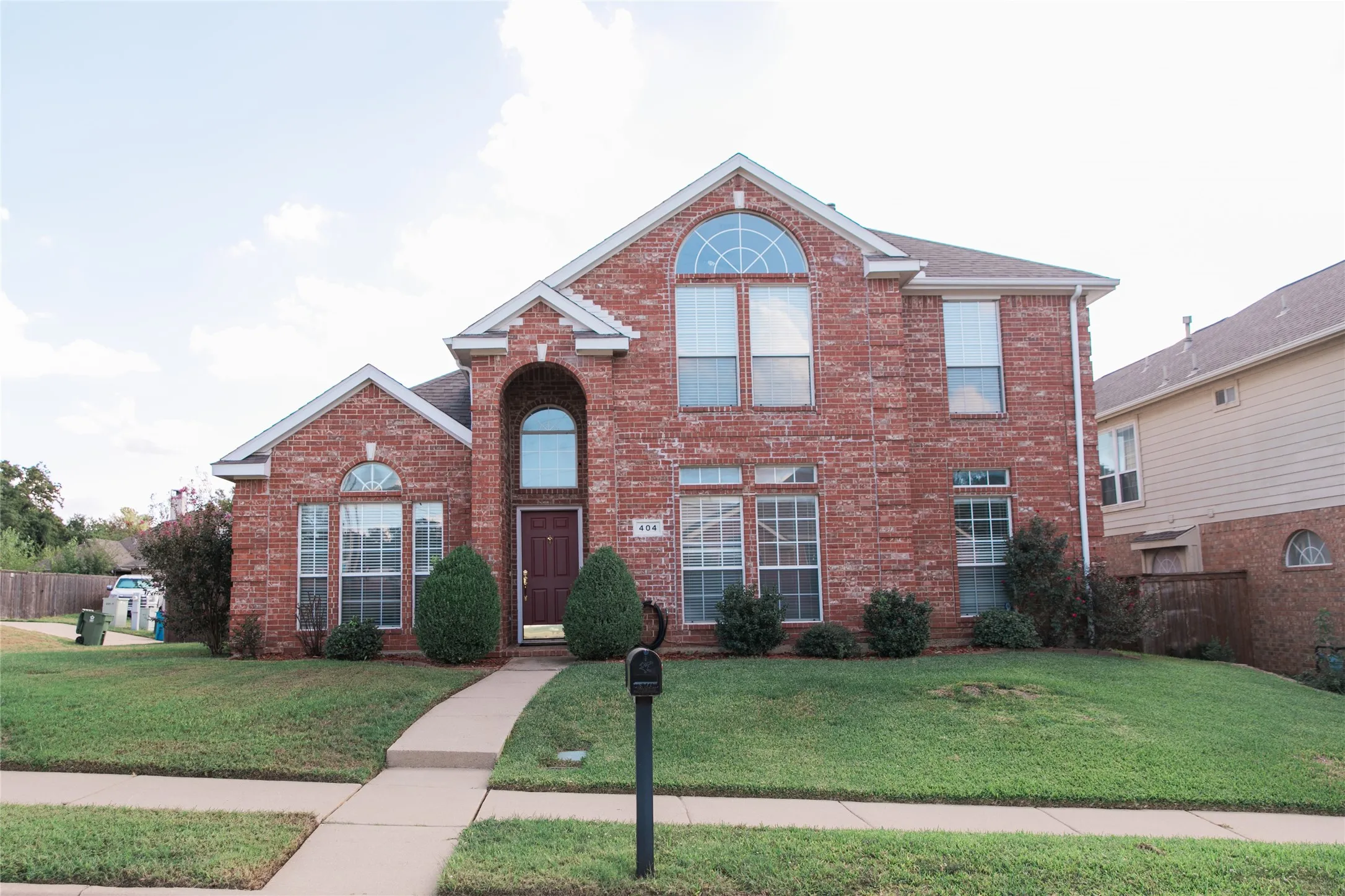 Two-story brick exterior featuring an arched entryway, decorative fanlight windows, and a multi-gabled roofline