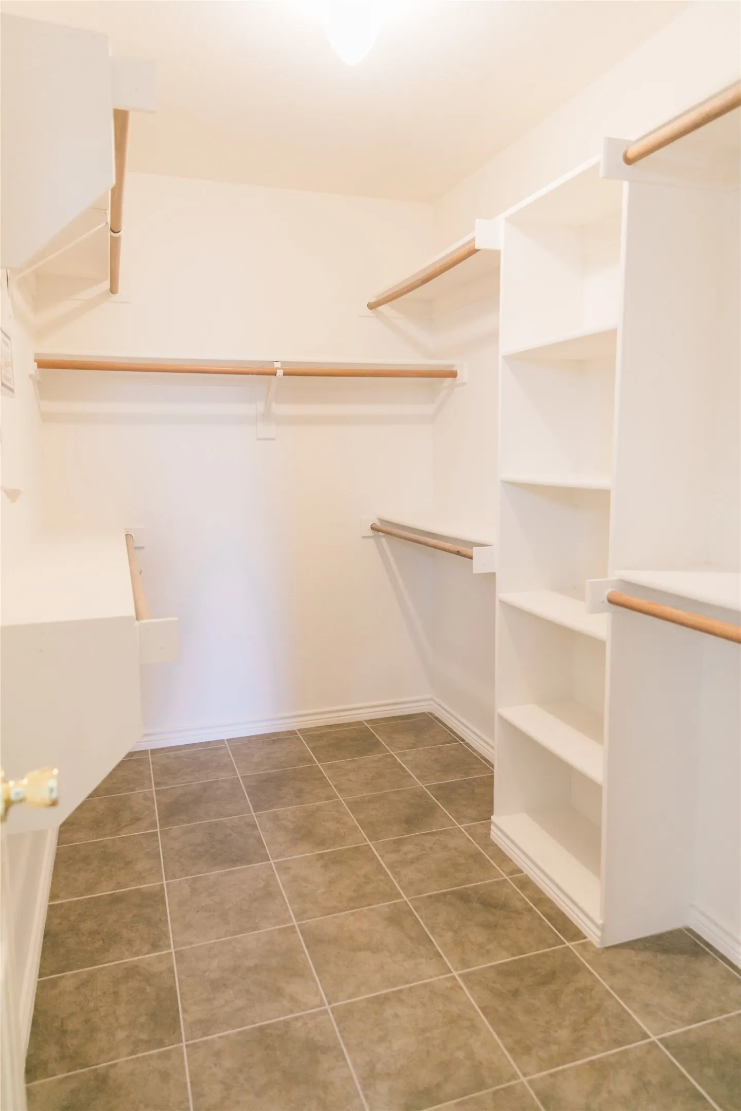 Walk-in closet featuring white built-in shelving, wooden garment rods, and ceramic tile flooring