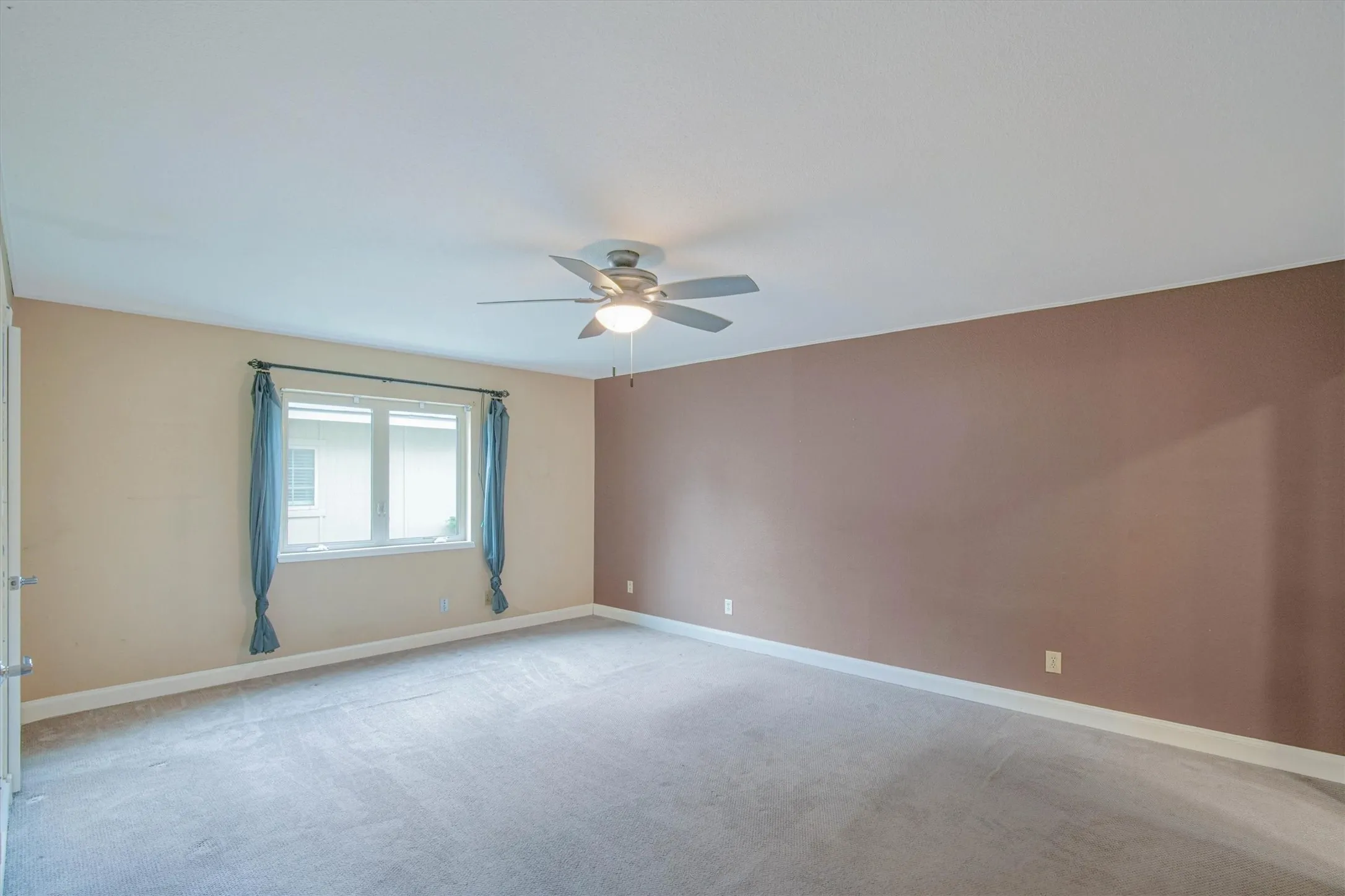 Interior space featuring neutral wall tones, a large window, wall-to-wall carpeting, and a ceiling-mounted light fixture with fan blades