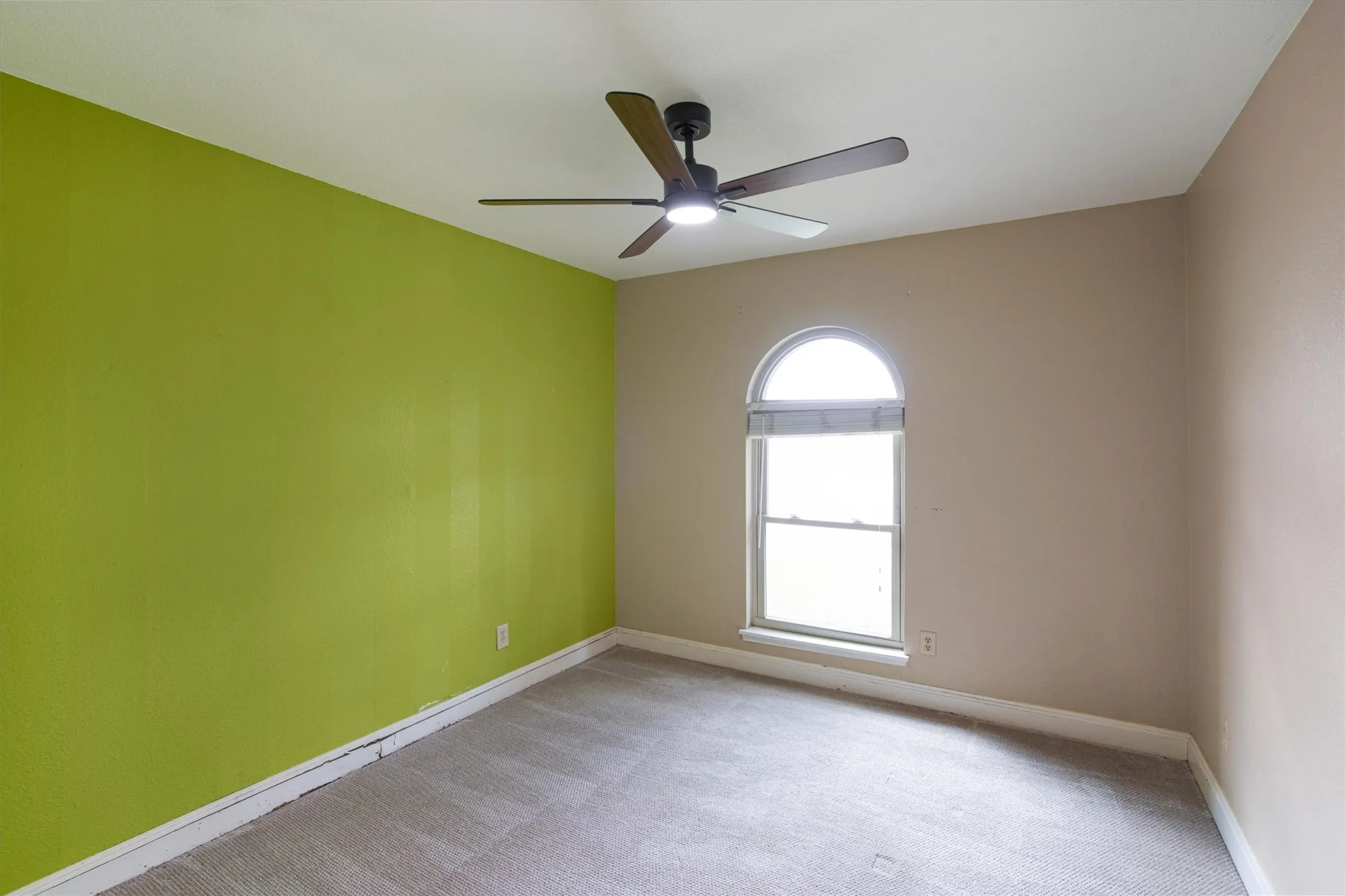 Interior room featuring wall-to-wall carpeting, an arched window, and a ceiling fan with integrated lighting