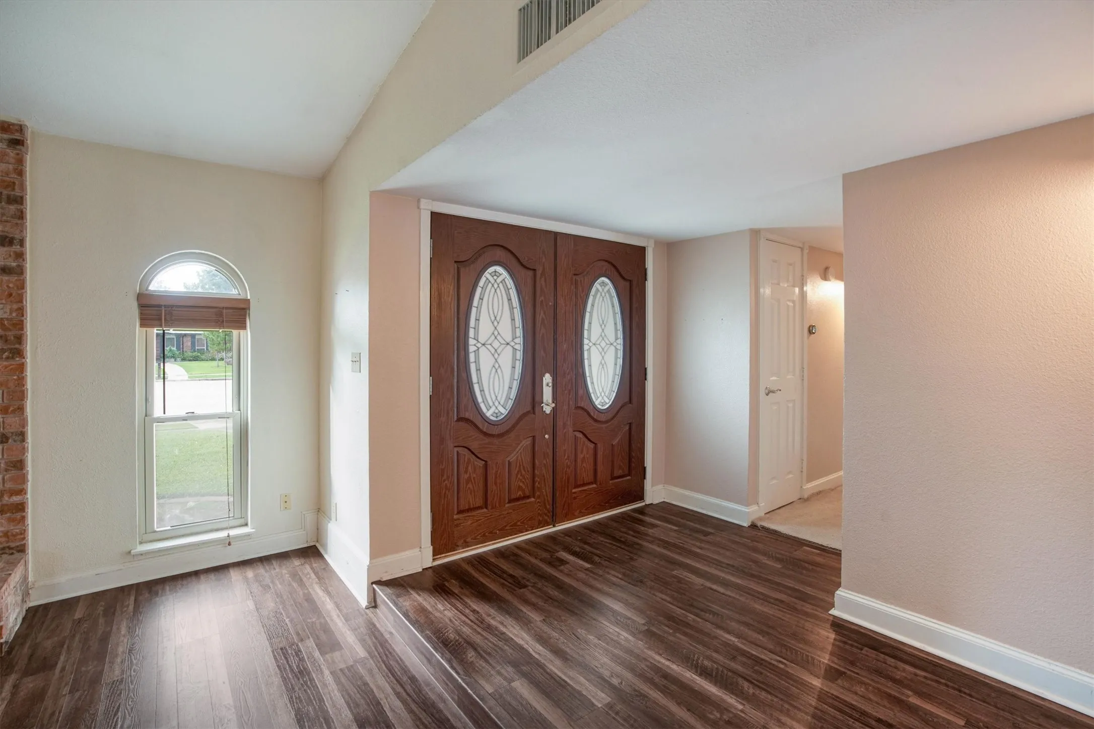 Double entry doors featuring oval glass inserts, vaulted ceiling, luxury vinyl plank flooring, and an arched window