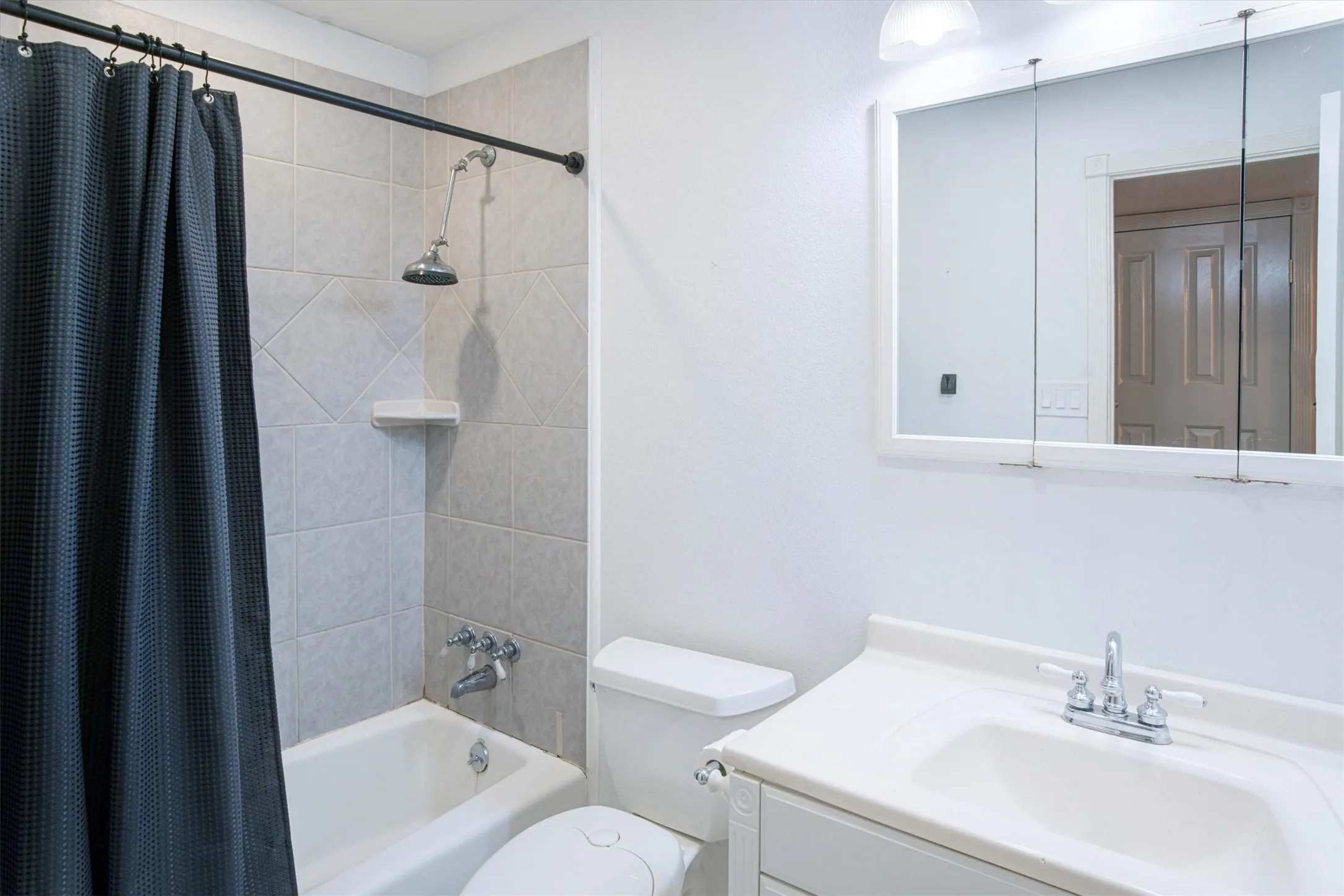 Bathroom featuring a porcelain tub with tile surround, built-in recessed shelf, vanity with an integrated sink, and wall-mounted medicine cabinet