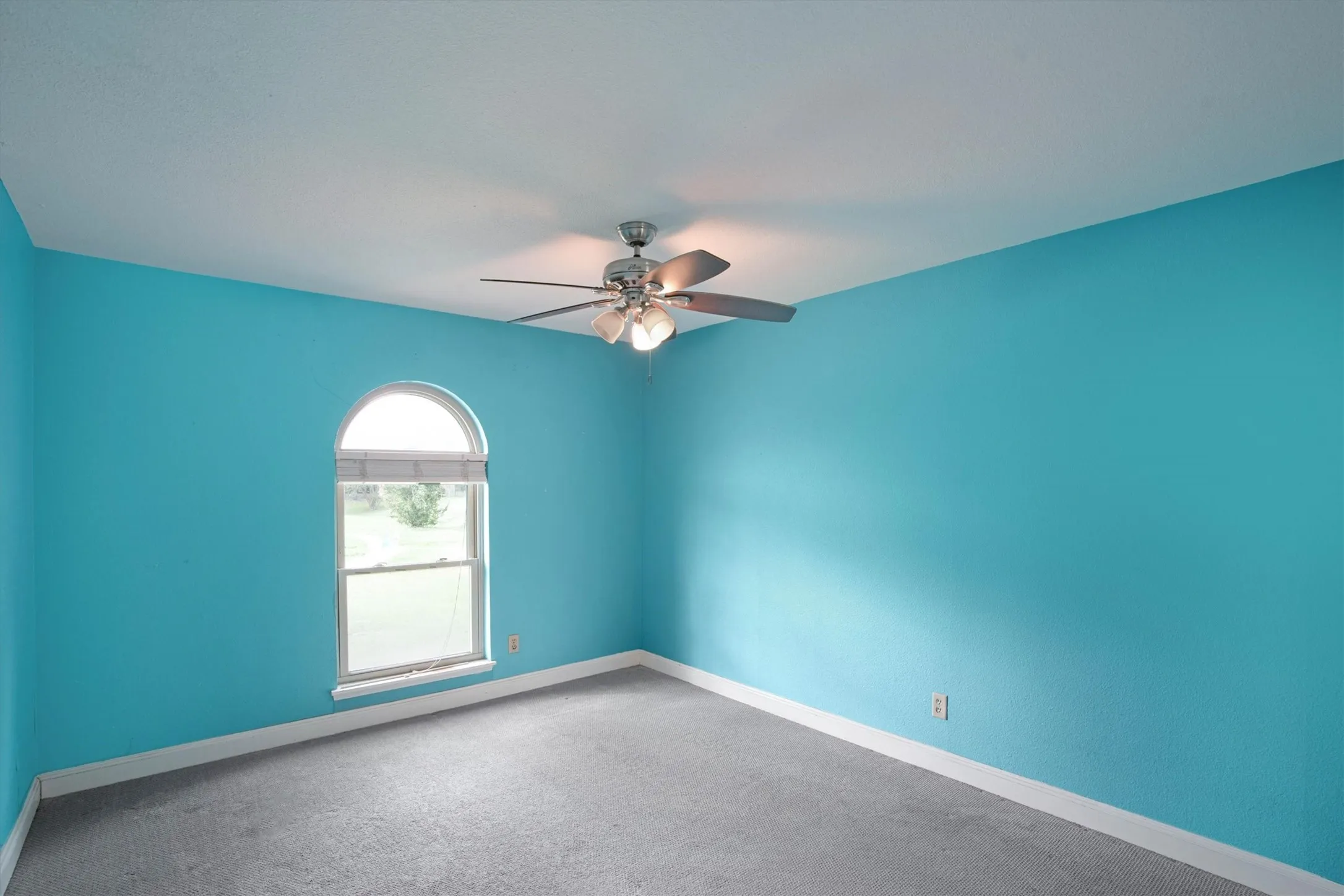 Room featuring an arched window, carpeted flooring, and a ceiling-mounted light fixture with a fan