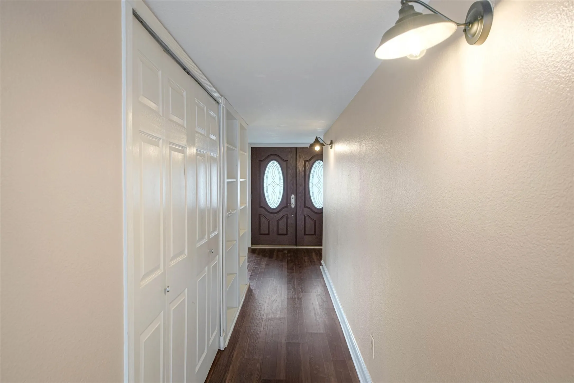 Entryway featuring double doors with oval glass inserts, luxury vinyl plank flooring, built-in shelving, utility closet, and industrial-style wall-mounted lighting fixtures