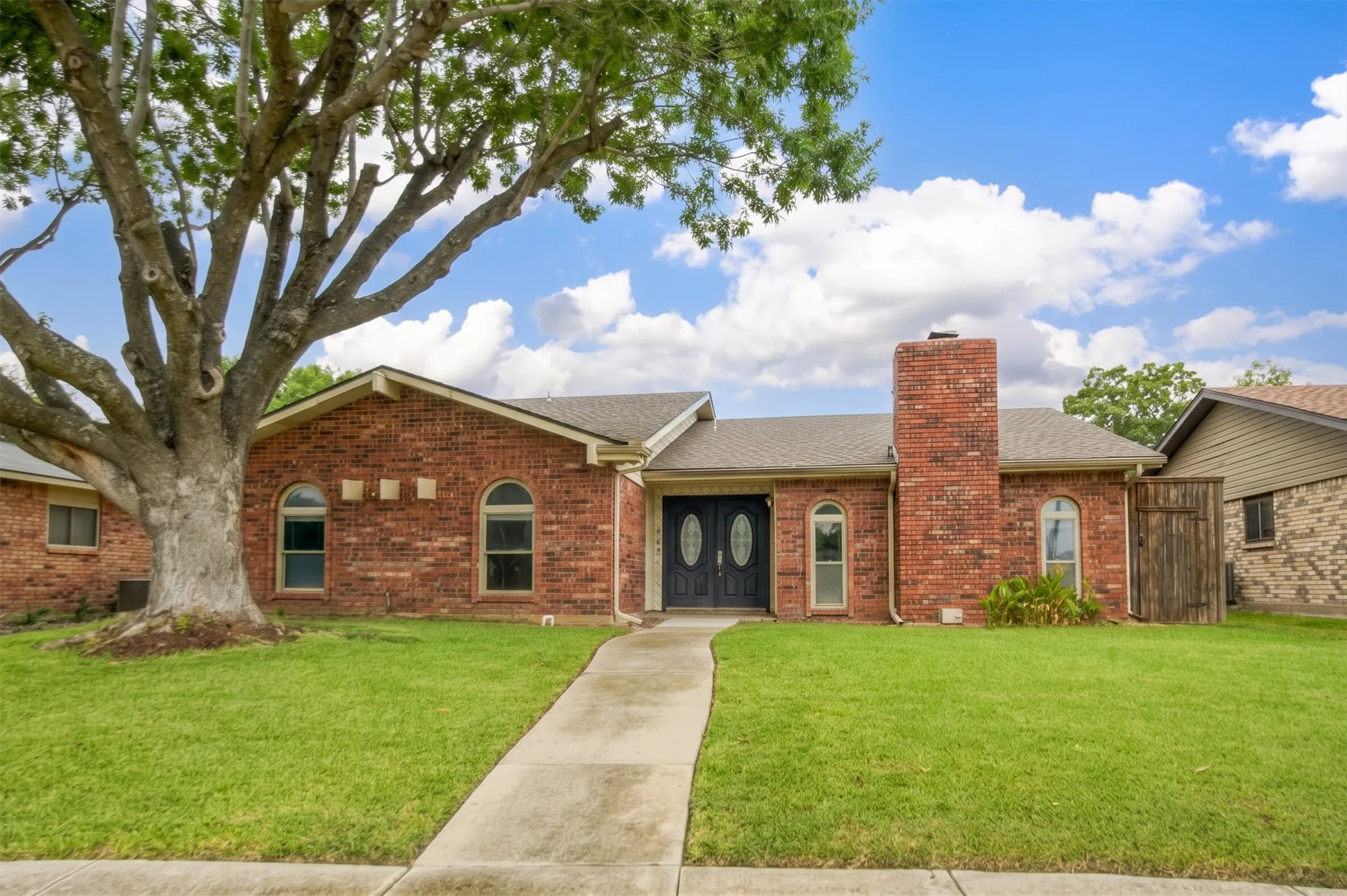 Single-story brick exterior featuring a prominent red brick chimney, arched windows, and a double-door entryway