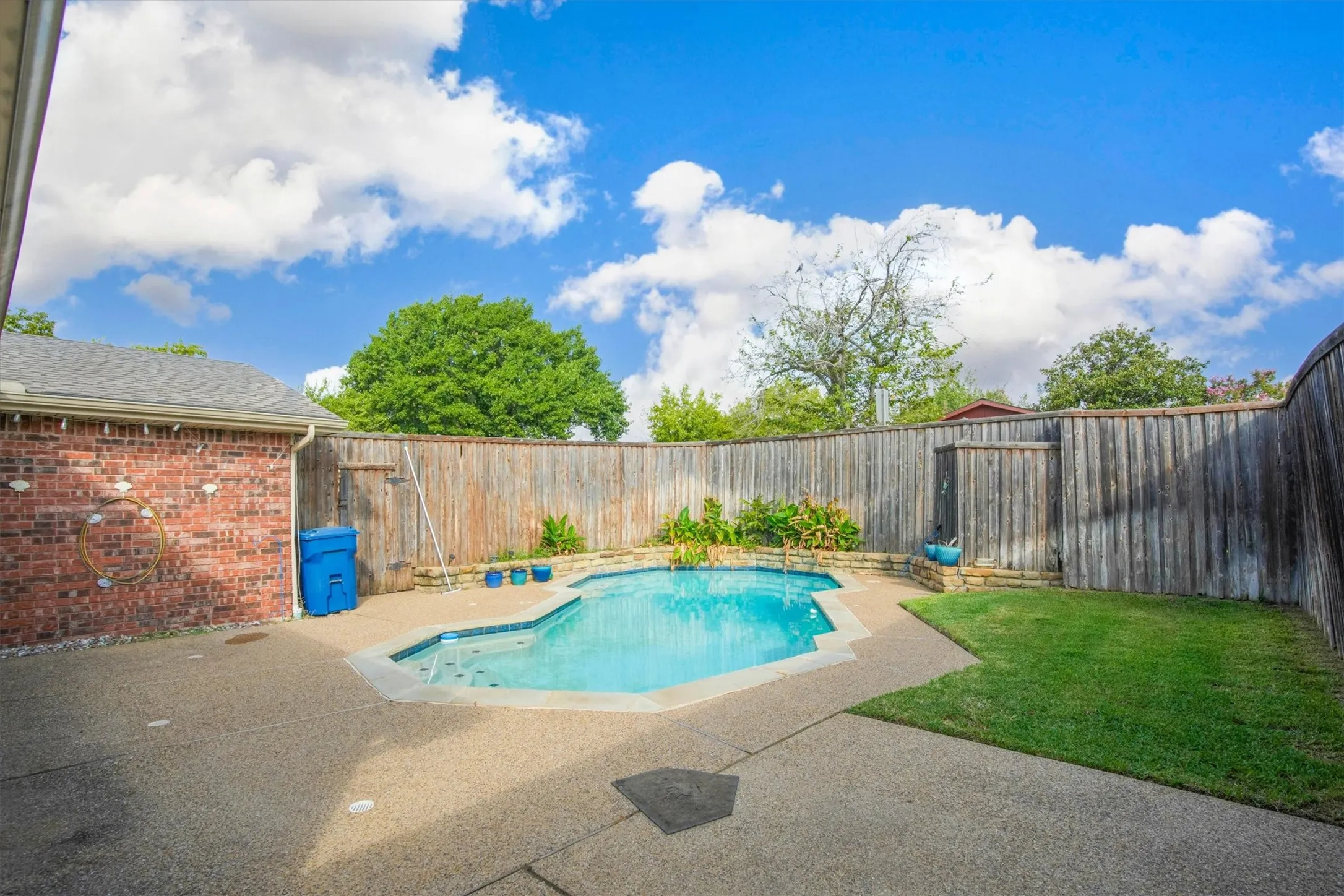 Outdoor space featuring a swimming pool, concrete patio, perimeter wood fencing, and a brick exterior wall