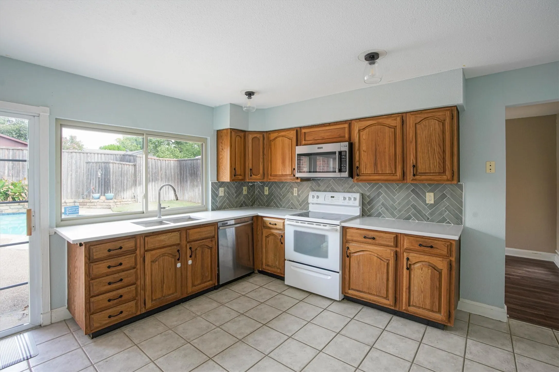 Kitchen featuring wood cabinetry, herringbone-pattern tile backsplash, stainless steel appliances, quartz countertops, and ceramic tile flooring