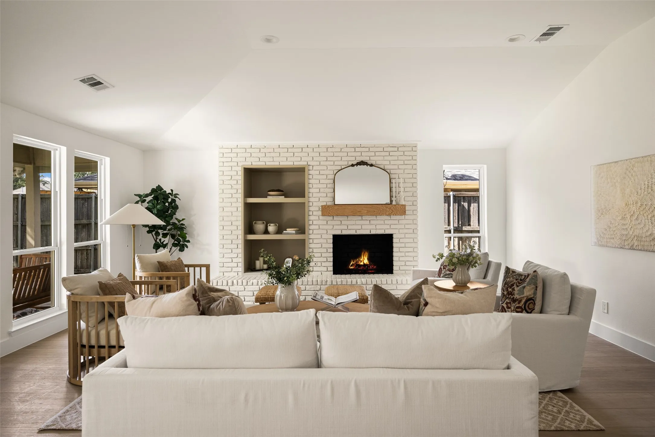 Bright and inviting living area featuring vaulted ceilings, a beautifully updated brick fireplace with wood mantel, built-in shelving, and large windows overlooking the backyard.