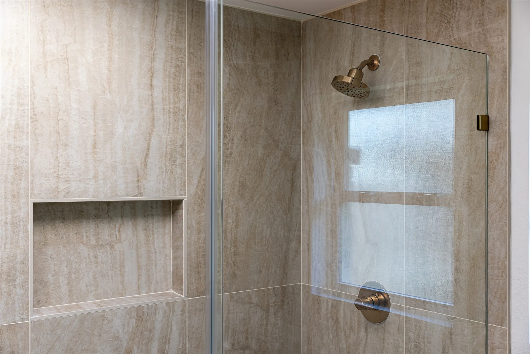Spa-inspired primary bathroom featuring an expansive glass-enclosed shower with striking floor-to-ceiling tile, rich natural textures, and a seamless design that creates a serene, resort-like retreat.
