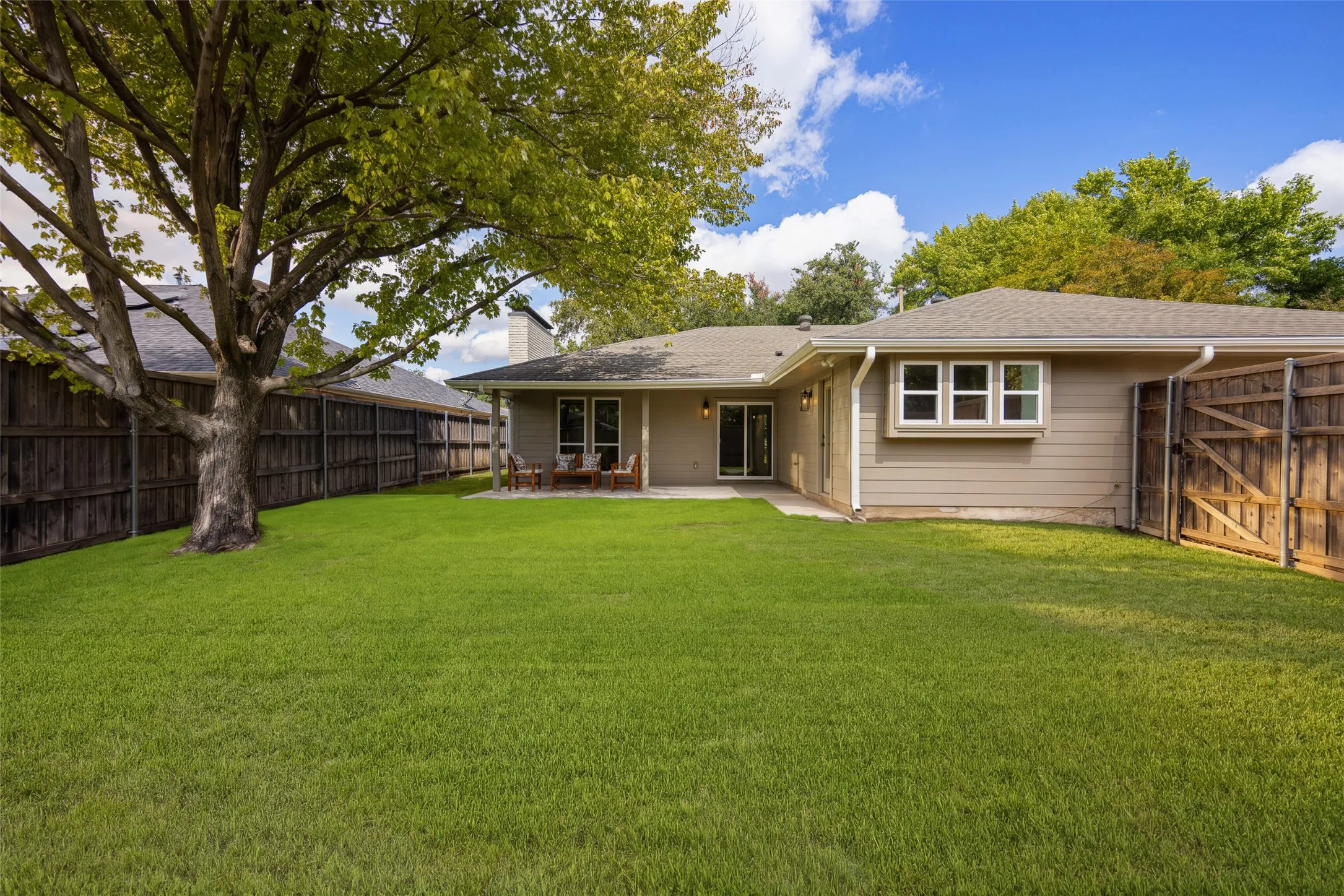 Expansive backyard with a spacious lawn, mature shade trees, privacy fencing, and a covered patio perfect for outdoor entertaining.