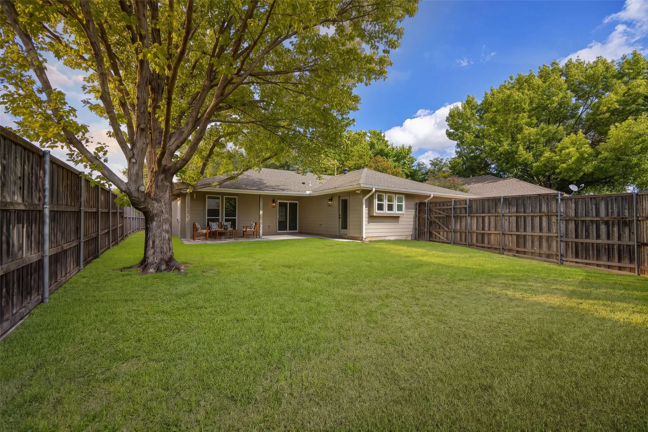 Expansive backyard with a spacious lawn, mature shade trees, privacy fencing, and a covered patio perfect for outdoor entertaining.
