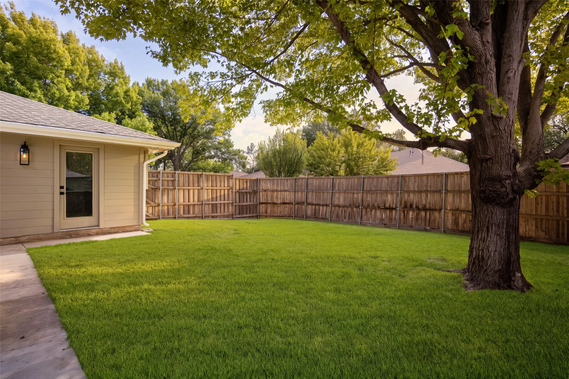 Expansive backyard with a spacious lawn, mature shade trees, privacy fencing, and a covered patio perfect for outdoor entertaining.