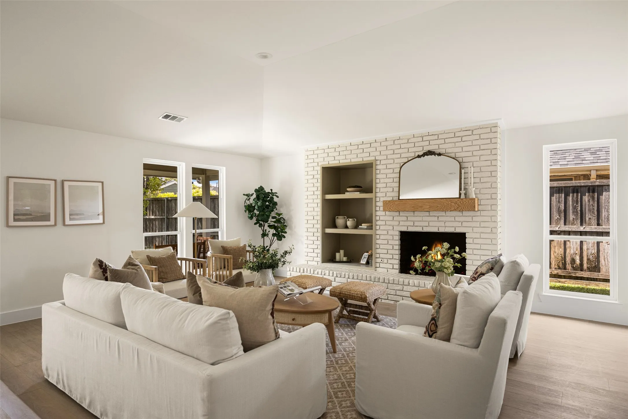 Bright and inviting living area featuring vaulted ceilings, a beautifully updated brick fireplace with wood mantel, built-in shelving, and large windows overlooking the backyard.