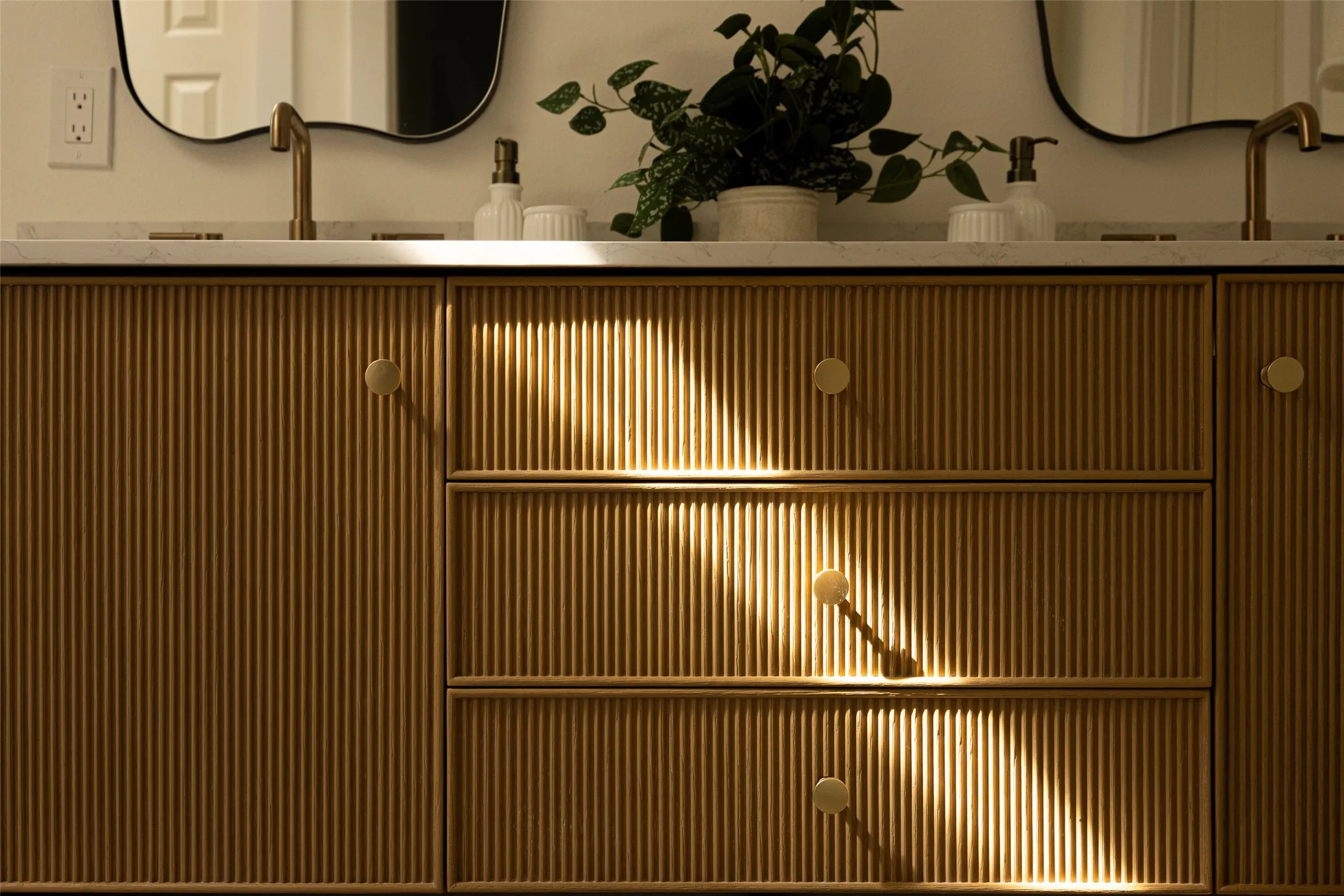 Luxuriously updated primary bathroom featuring a striking fluted wood double vanity, elegant brass fixtures, and designer mirrors.