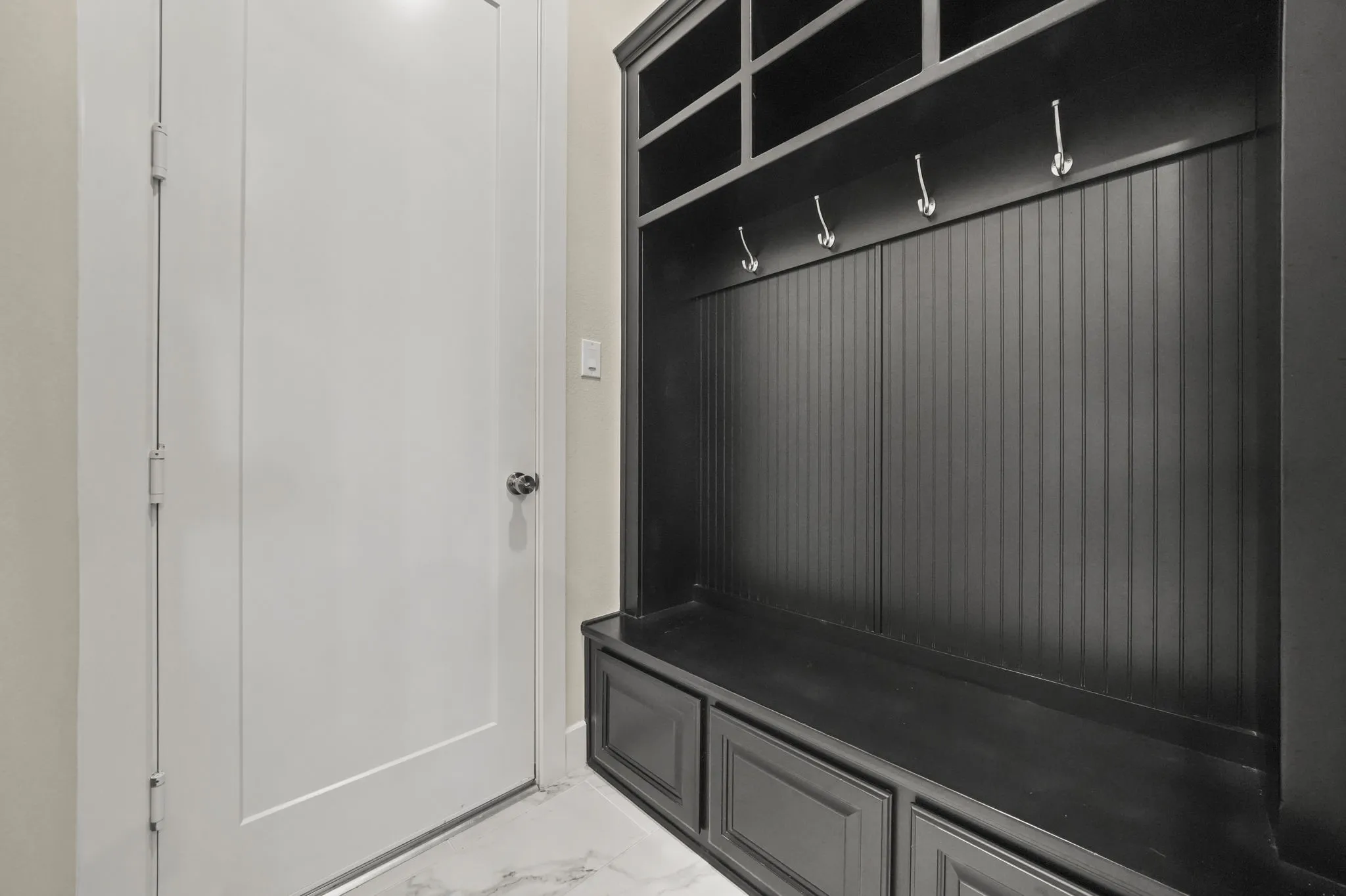 Built-in mudroom cabinetry featuring dark finish shaker-style lower drawers, beadboard paneling, integrated upper shelving, and metallic hooks, set against light-toned flooring
