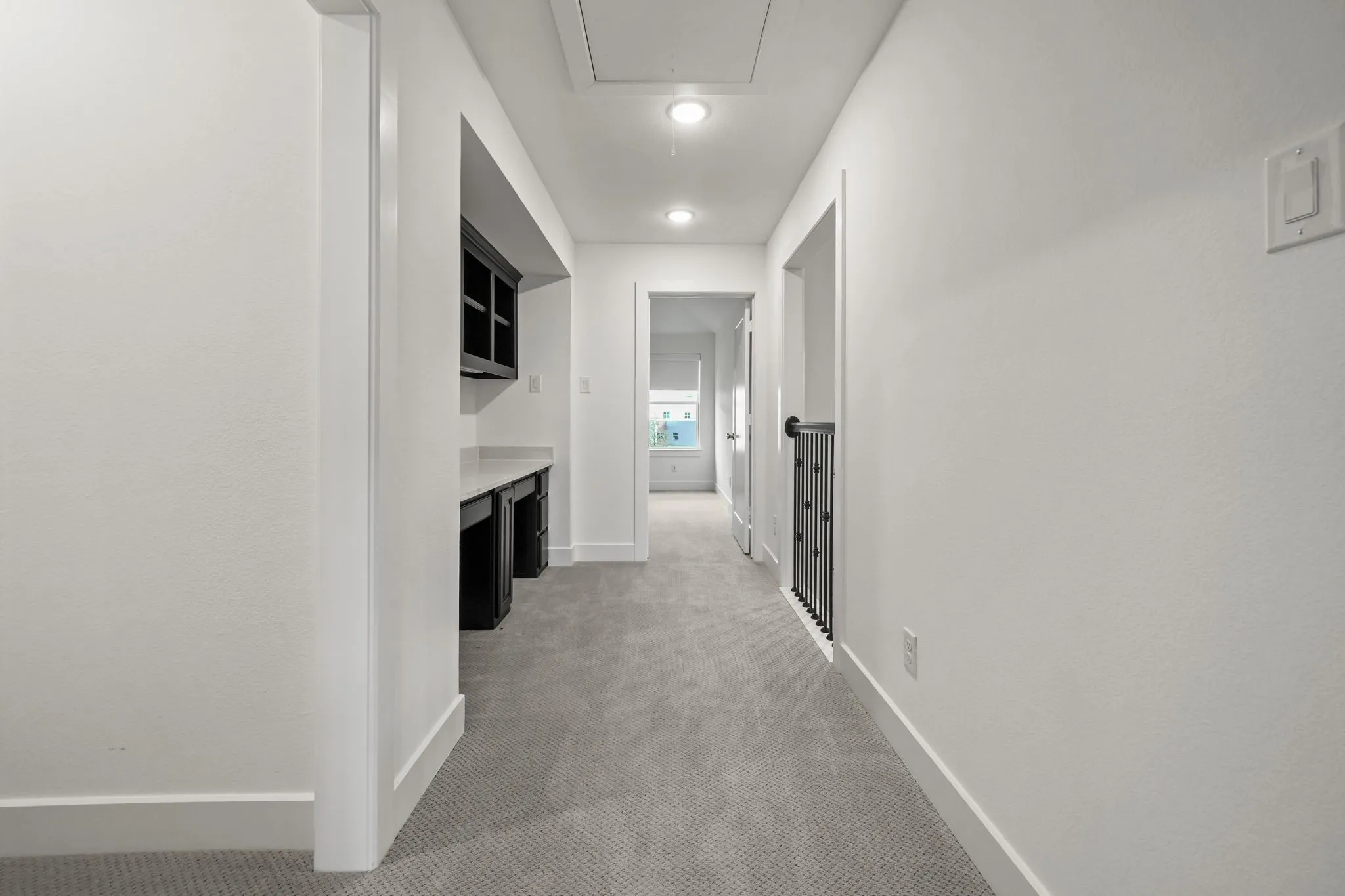 Hallway featuring wall-to-wall carpeting, built-in desk with dark cabinetry and stone-surface countertop, overhead recessed lighting, and metal stair railing