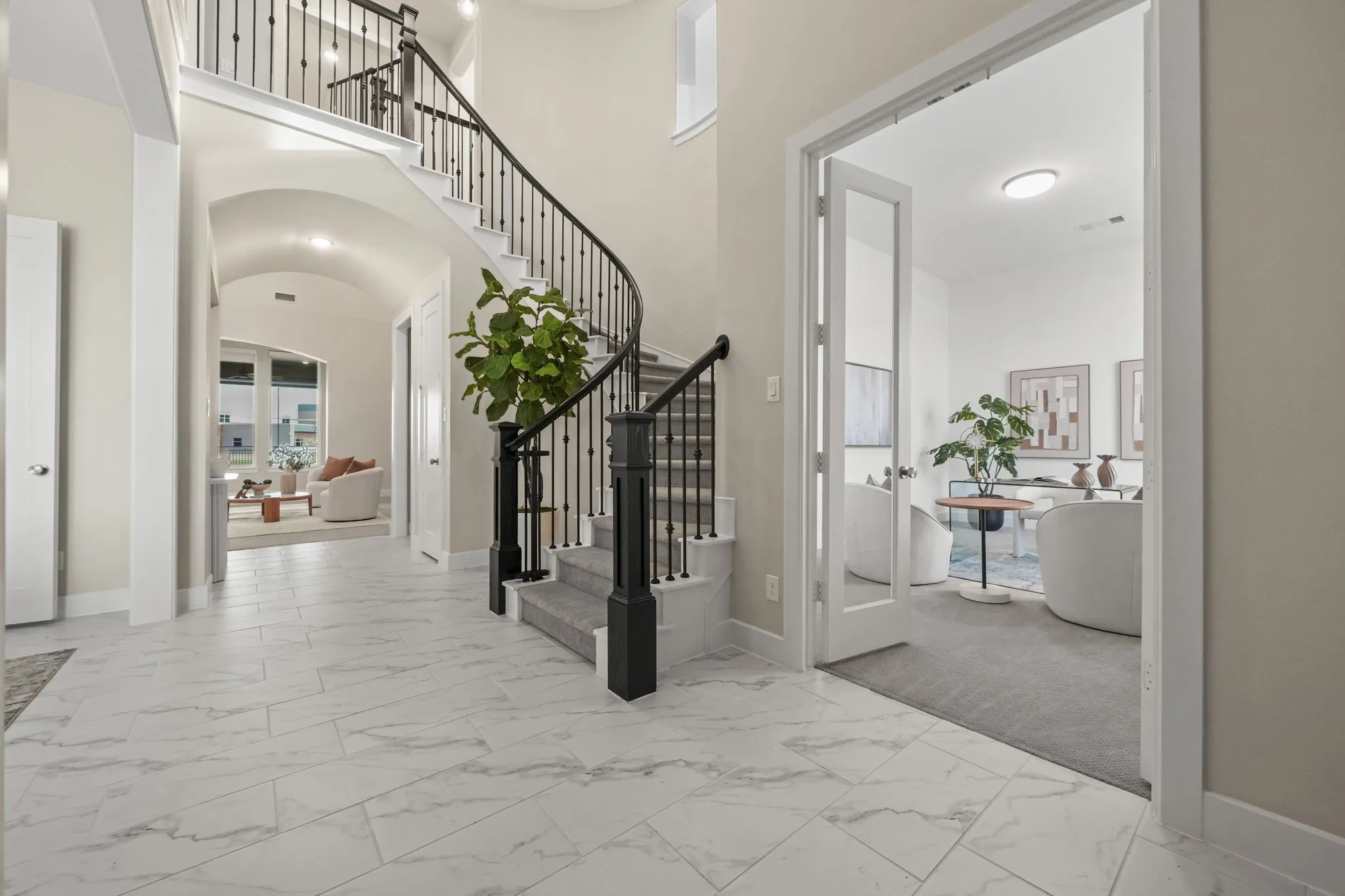 Grand foyer featuring large-format tile flooring, a curved staircase with wrought-iron balusters, an arched hallway, and a glass-paned French door entry to an auxiliary room