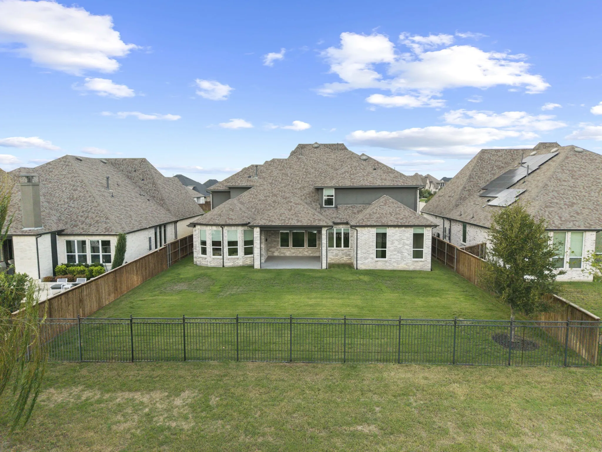 Rear exterior featuring light-toned masonry, a covered patio, multiple multi-pane windows, a fenced backyard, and a composition shingle roof