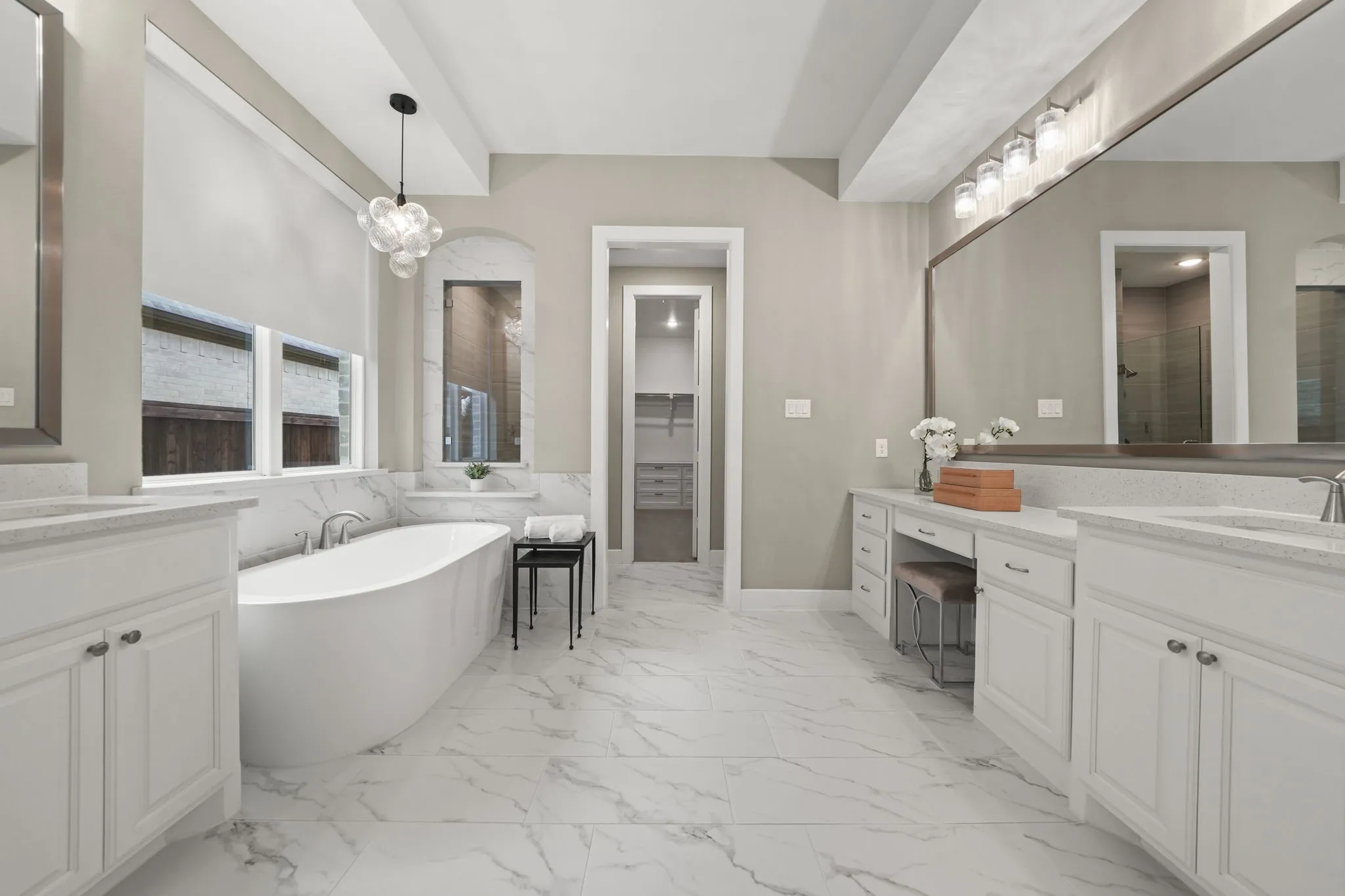 Bathroom featuring dual white vanities with stone-surface countertops, a freestanding soaking tub, large-format tile flooring, and a recessed vanity area