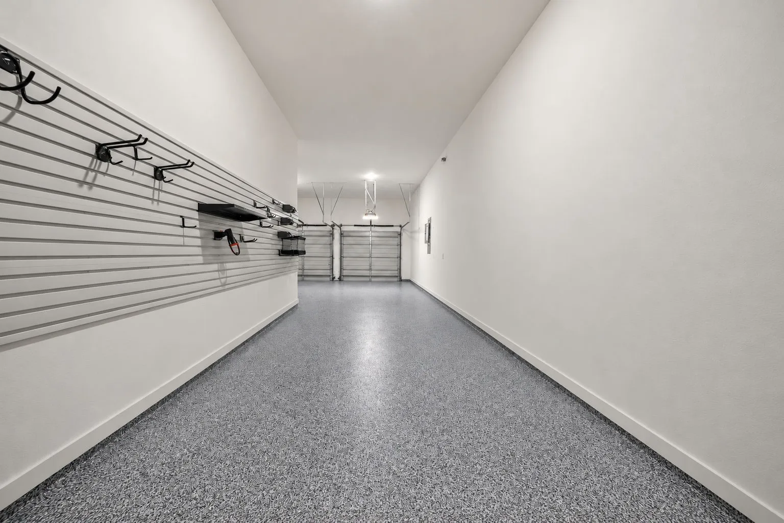 Garage featuring epoxy-coated flooring, heavy-duty wall-mounted slat wall storage system, and dual metal roll-up doors