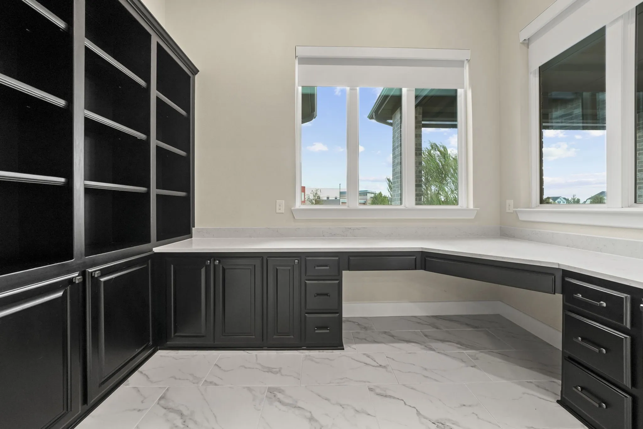 Built-in floor-to-ceiling cabinetry, L-shaped desk with stone countertop, large windows, and tile flooring