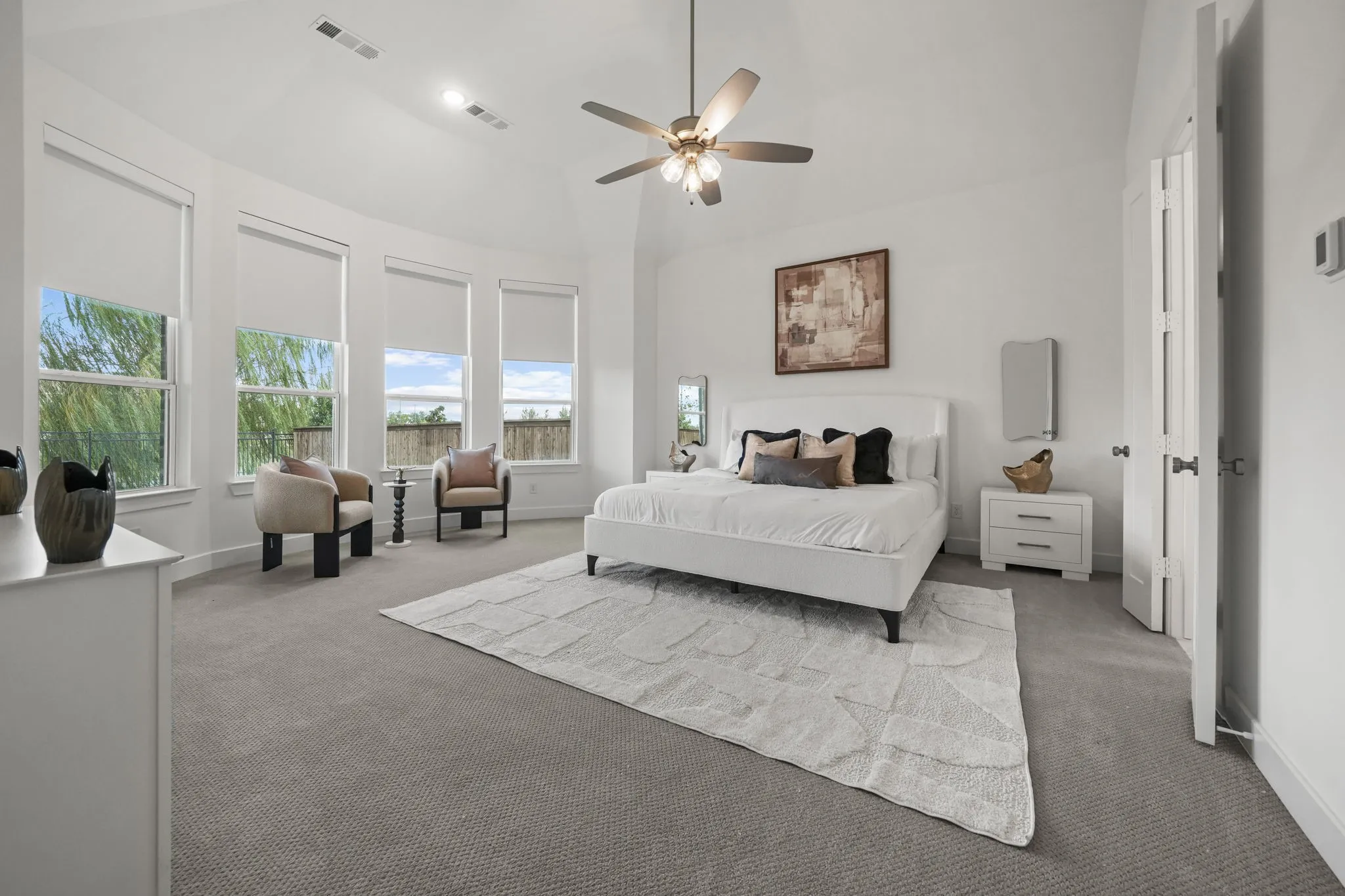 Vaulted ceiling, four-paneled bay window configuration, neutral carpeting, and a multi-blade ceiling fan with integrated lighting