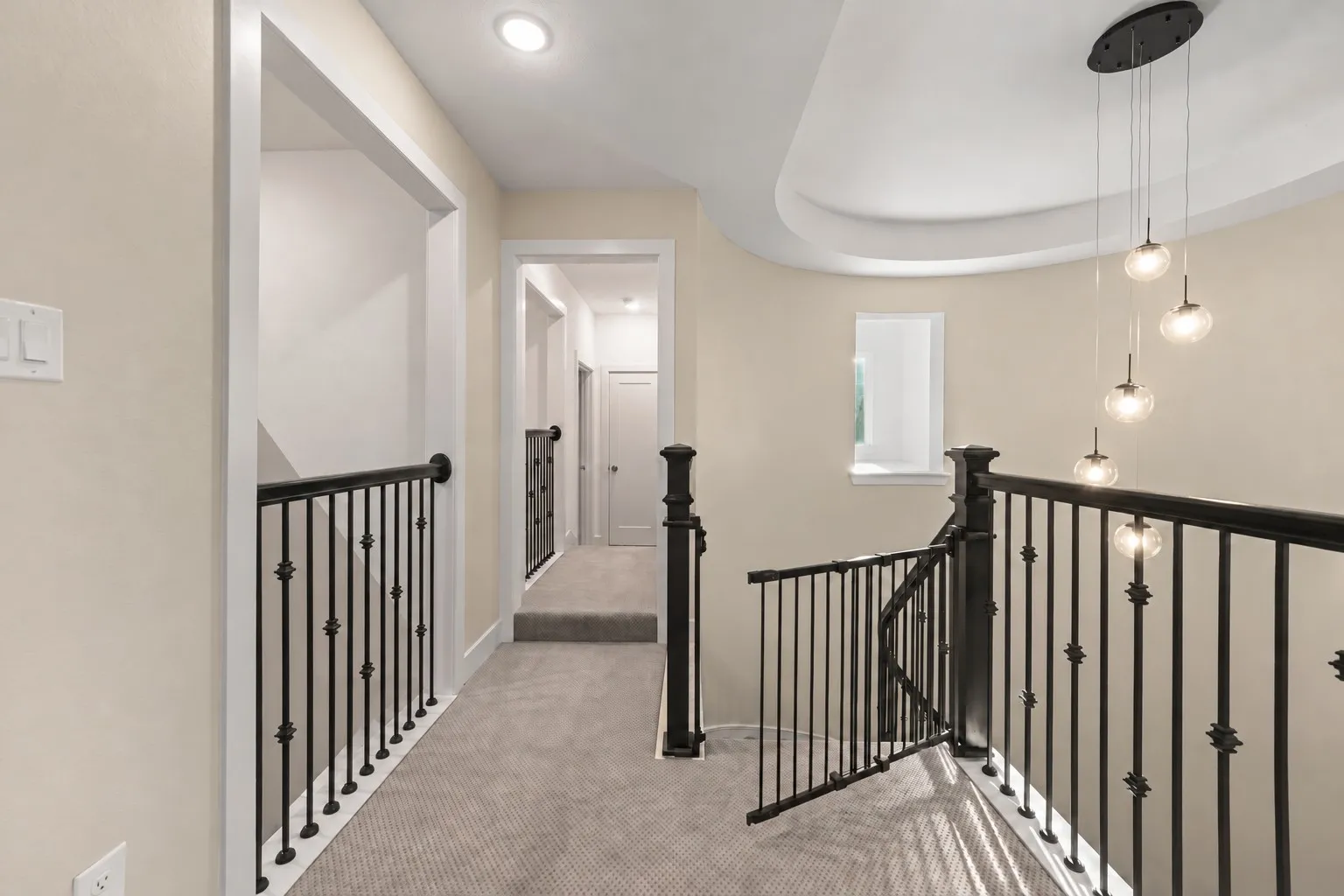 Neutral carpeting, wrought iron stair railing with ornate finials, tiered multi-globe pendant lighting, and recessed ceiling architecture