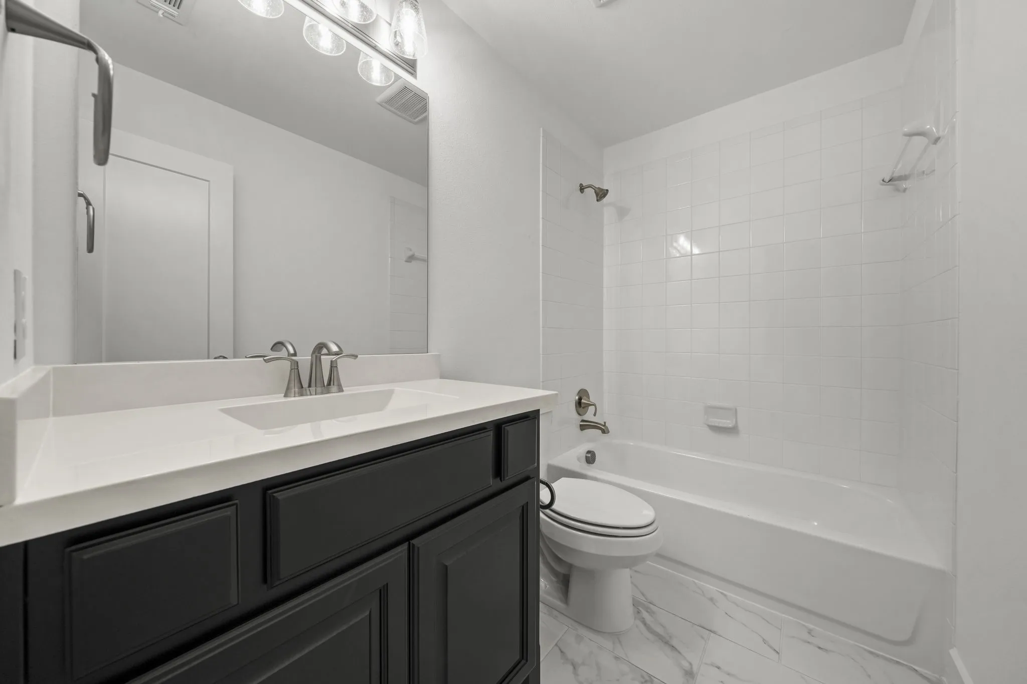 Dark-toned vanity with a solid-surface countertop, rectangular integrated sink, white tile shower surround, and patterned flooring