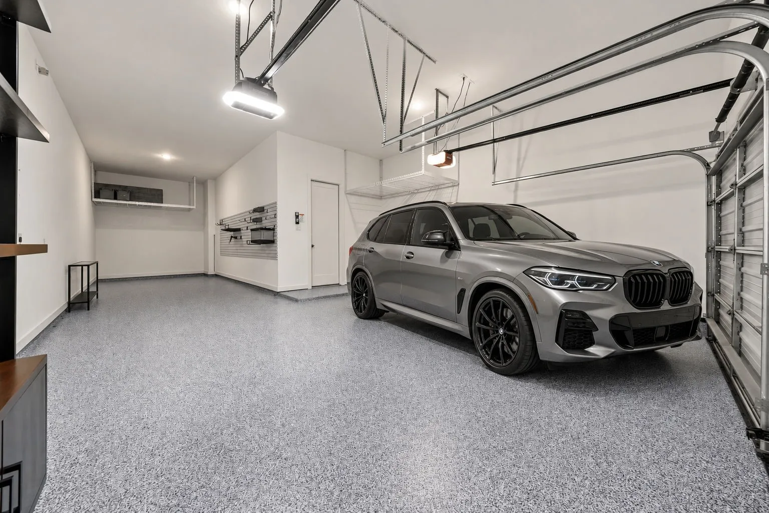 Spacious garage featuring high ceilings, epoxy-finished flooring, wall-mounted storage organization system, and overhead wire shelving